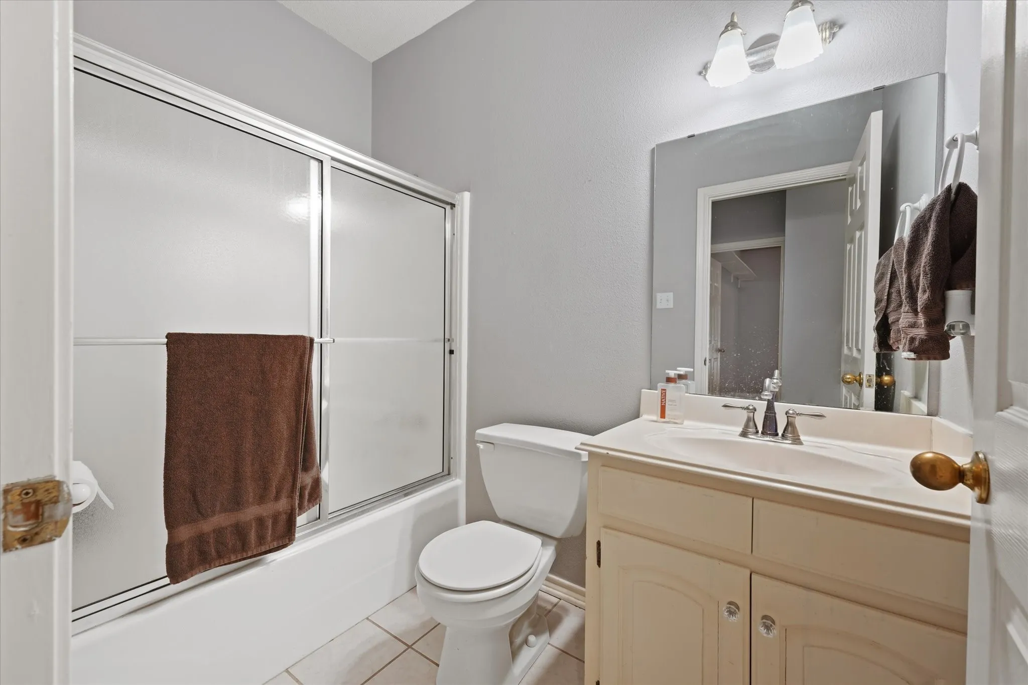 Bathroom featuring a built-in vanity with integrated sink, wall-mounted mirror, overhead two-light fixture, and tub with sliding glass enclosure