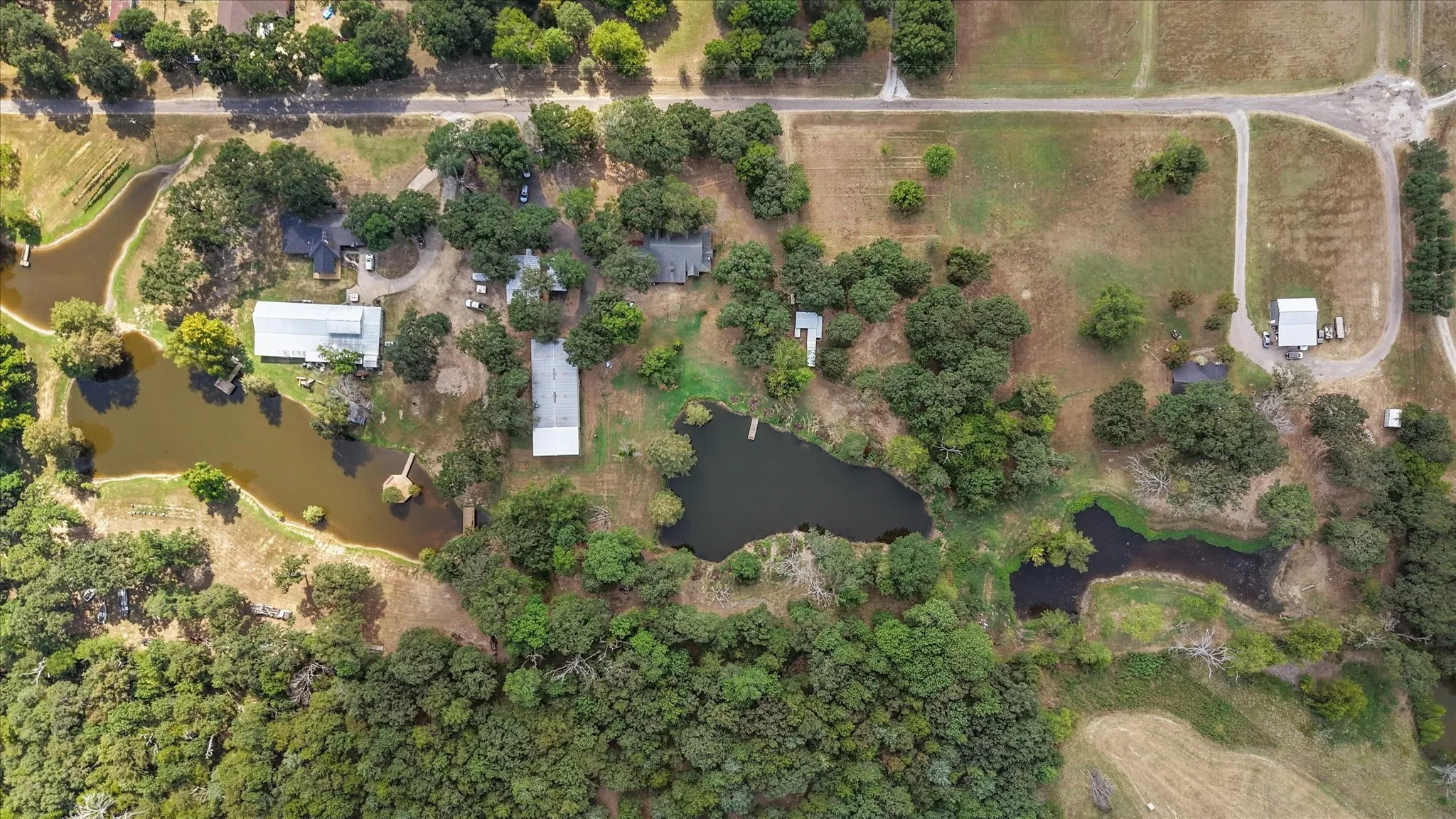 Expansive property featuring three distinct ponds, mature tree coverage, and multiple outbuildings