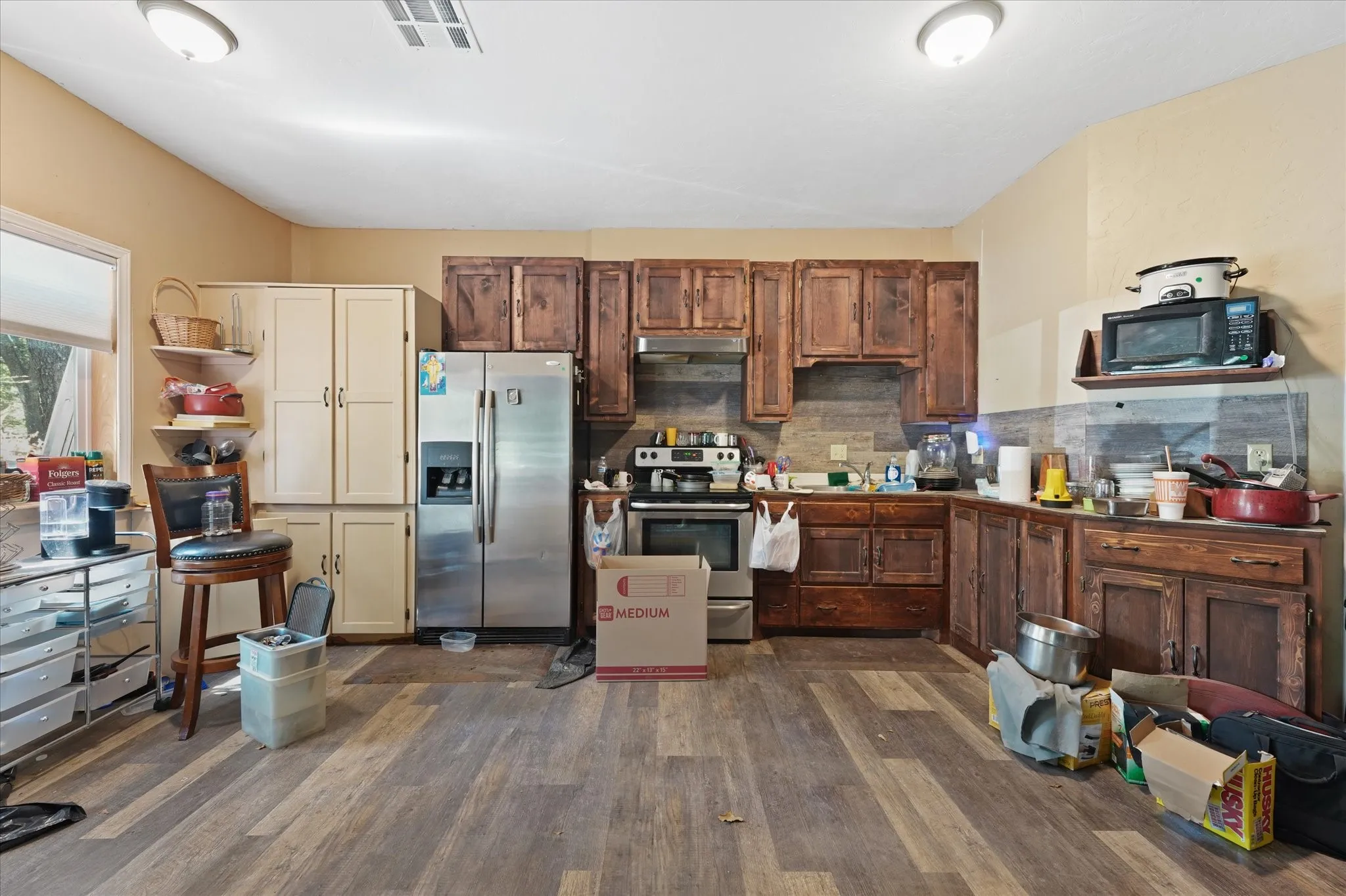 Wood-finish flooring, stainless steel refrigerator, and wood cabinetry with a tile-look backsplash