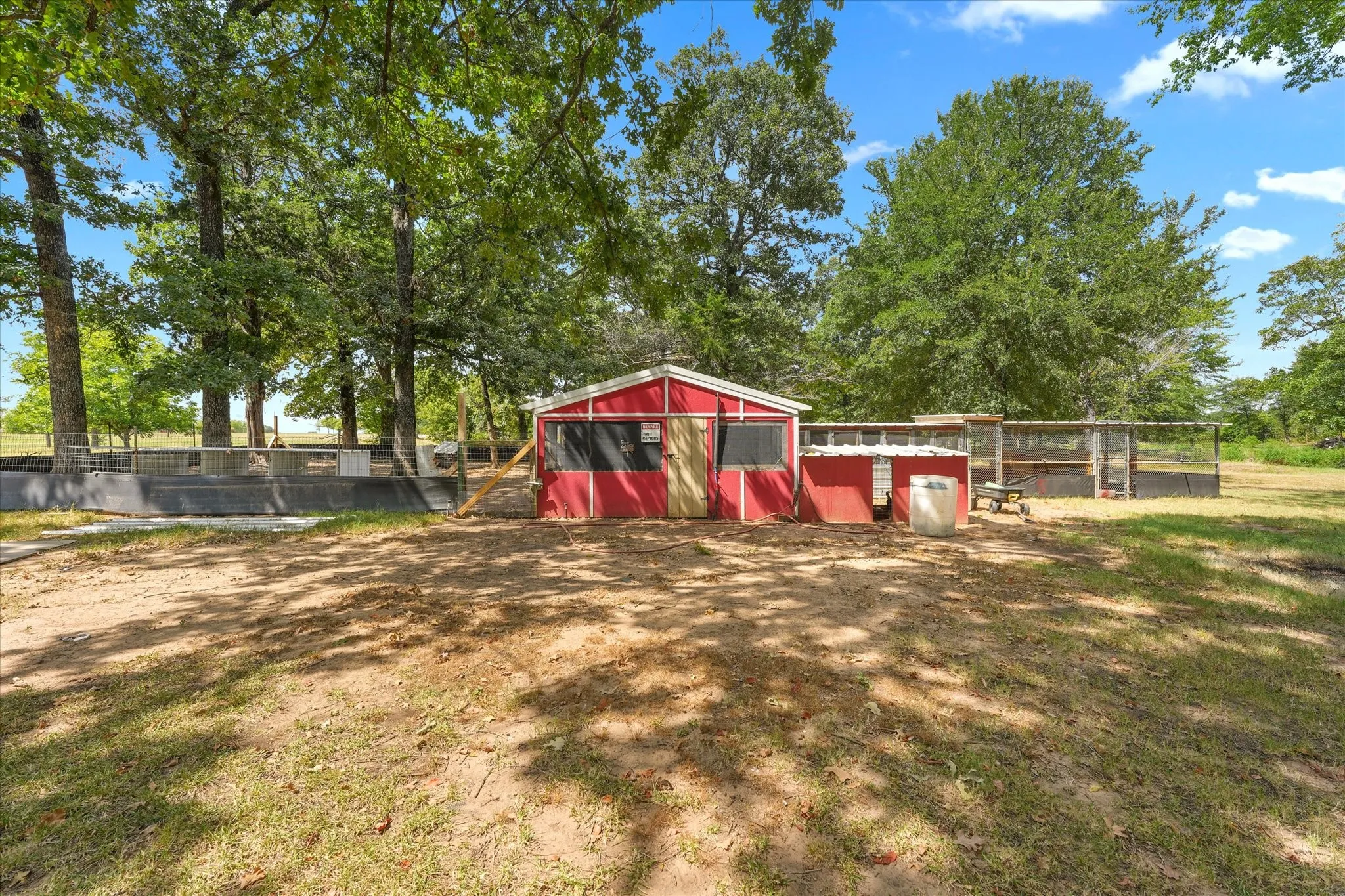 Red shed structure with a window, surrounded by fenced enclosures and mature trees