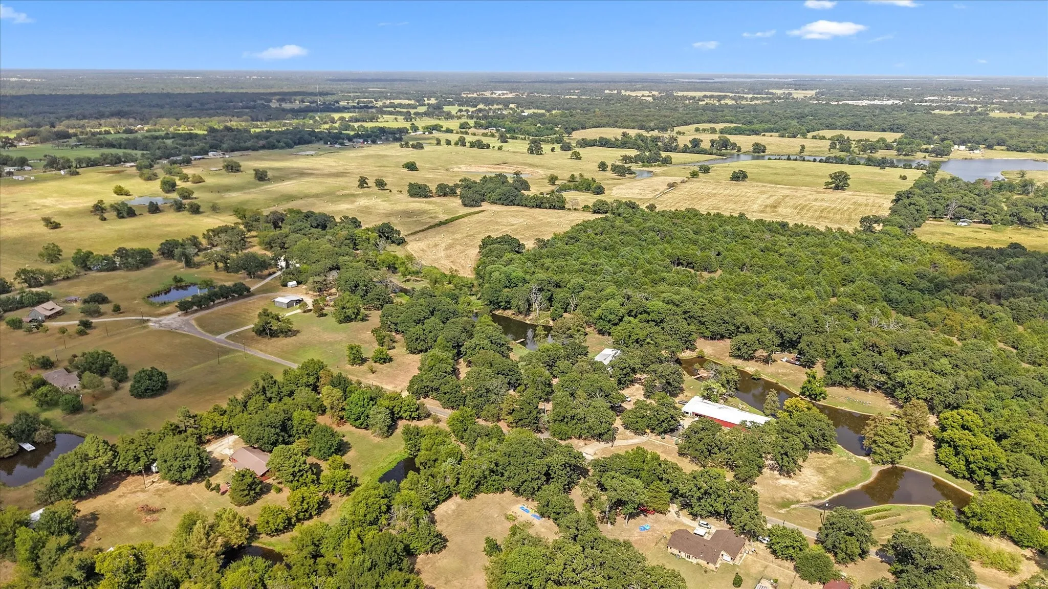 Expansive rural landscape featuring scattered homes, mature tree coverage, multiple ponds, and open fields