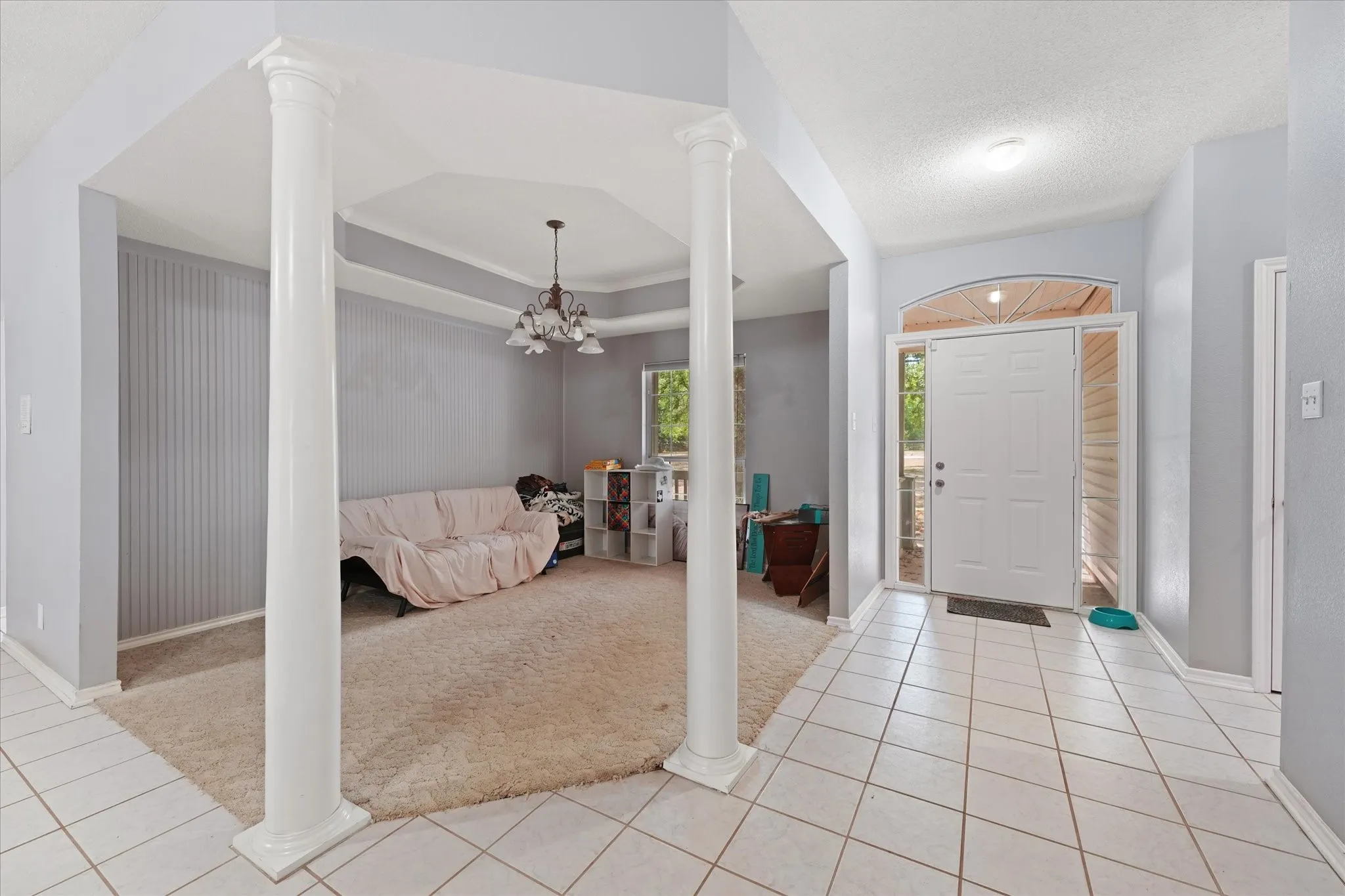 Tiled entry flooring, architectural columns, tray ceiling with chandelier, and a front door with transom and sidelight windows
