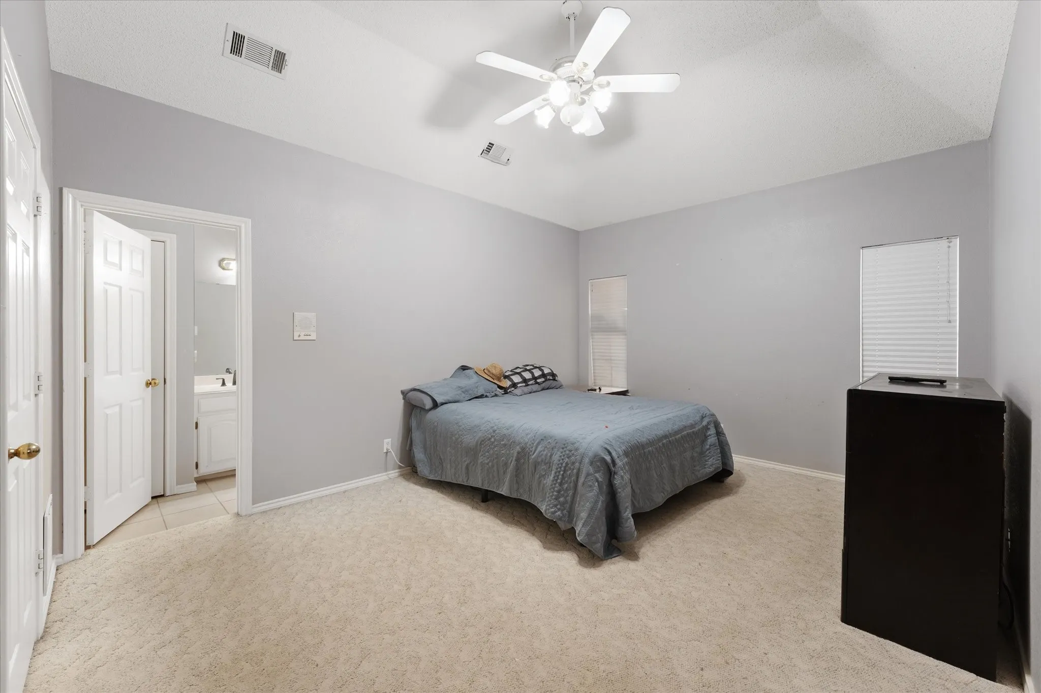 Vaulted ceiling, ceiling fan with light fixture, two windows with blinds, and light-toned carpet flooring
