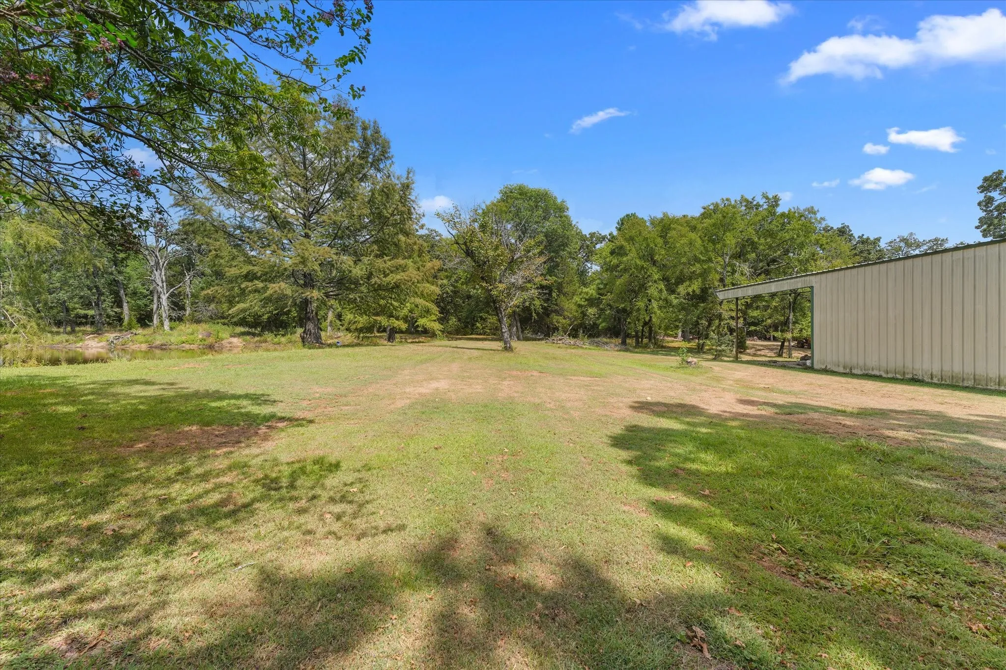 Expansive grassy area with mature trees and a metal-sided outbuilding