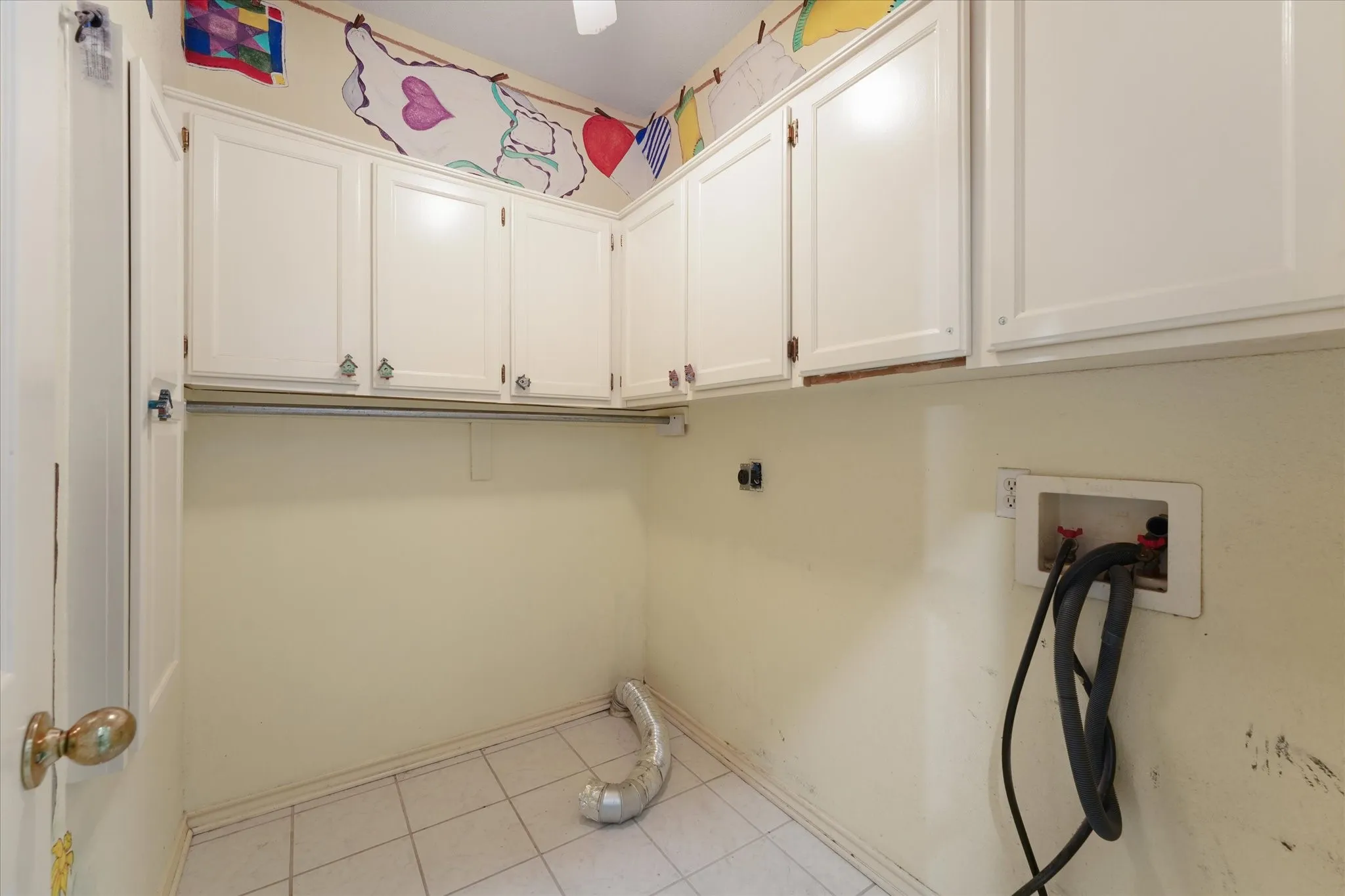 White shaker-style cabinetry with decorative hardware, tiled flooring, and a utility hook-up