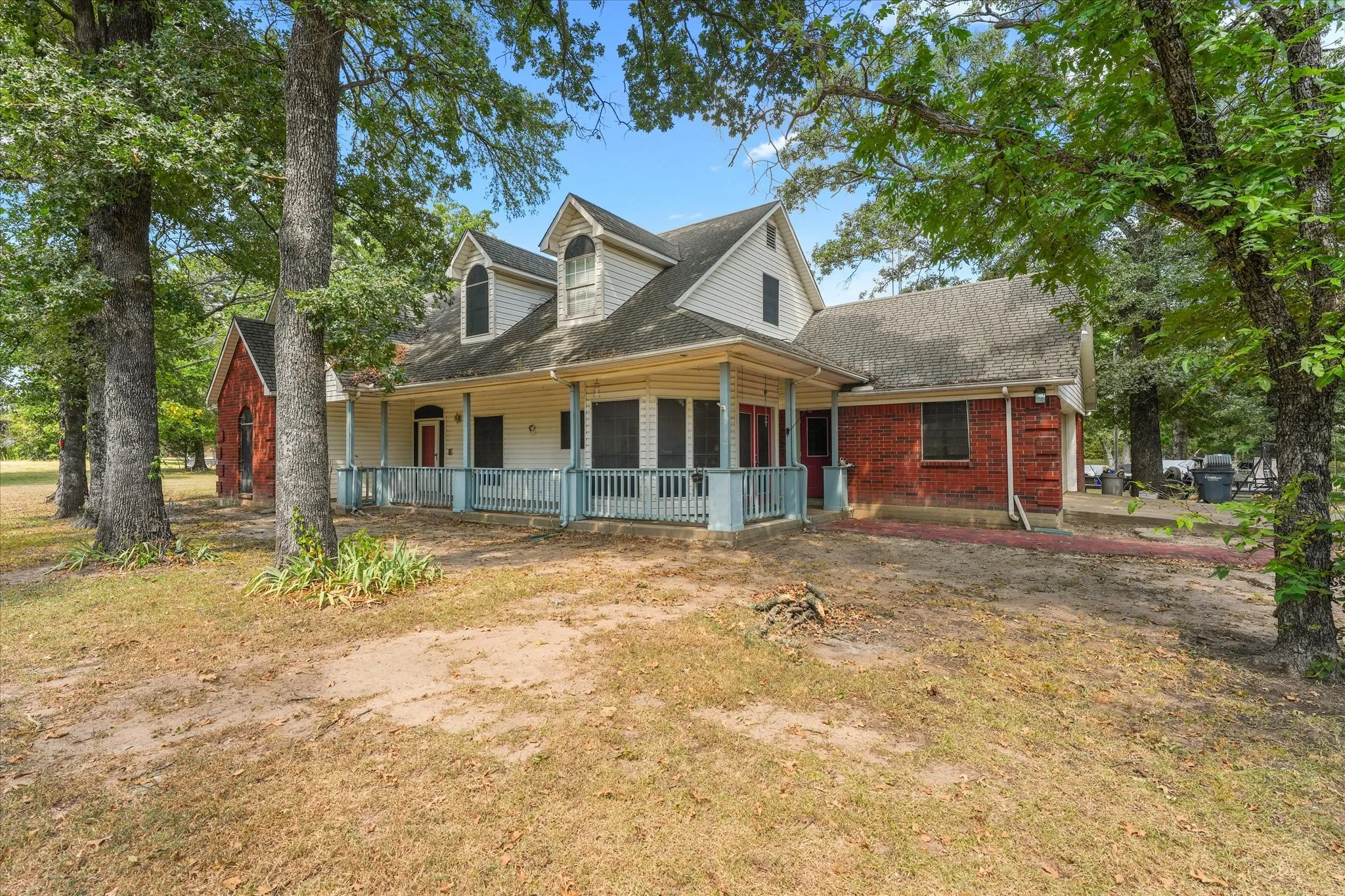 Exterior featuring dormer windows, a covered front porch with light blue railings, white siding, and red brick accents
