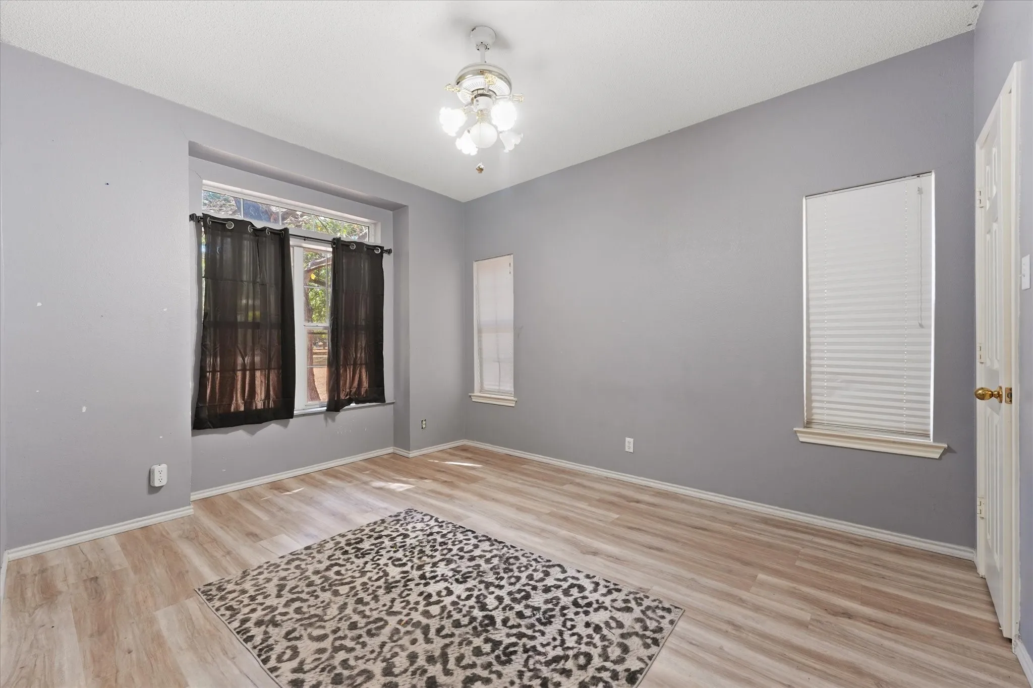 Recessed window framing, wood-finish flooring, ceiling-mounted light fixture, multiple windows, and light gray wall finish