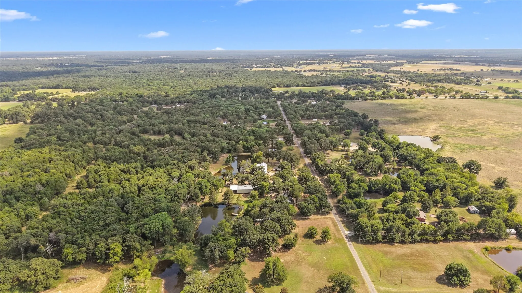 Expansive rural landscape featuring lush tree coverage, multiple ponds, and open fields