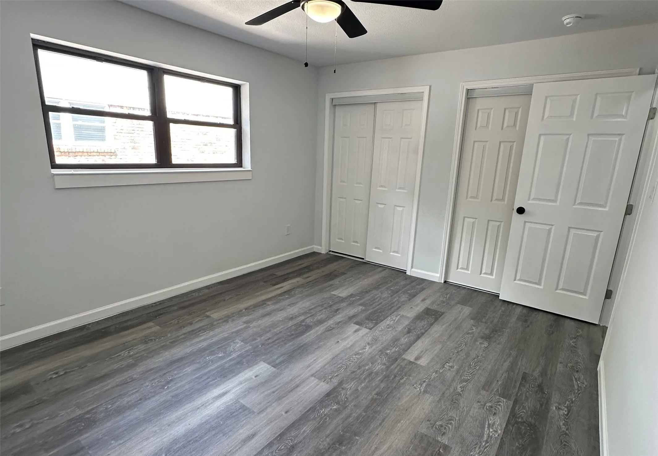 Wood-finish flooring throughout, bright window, ceiling fan, and two paneled doors