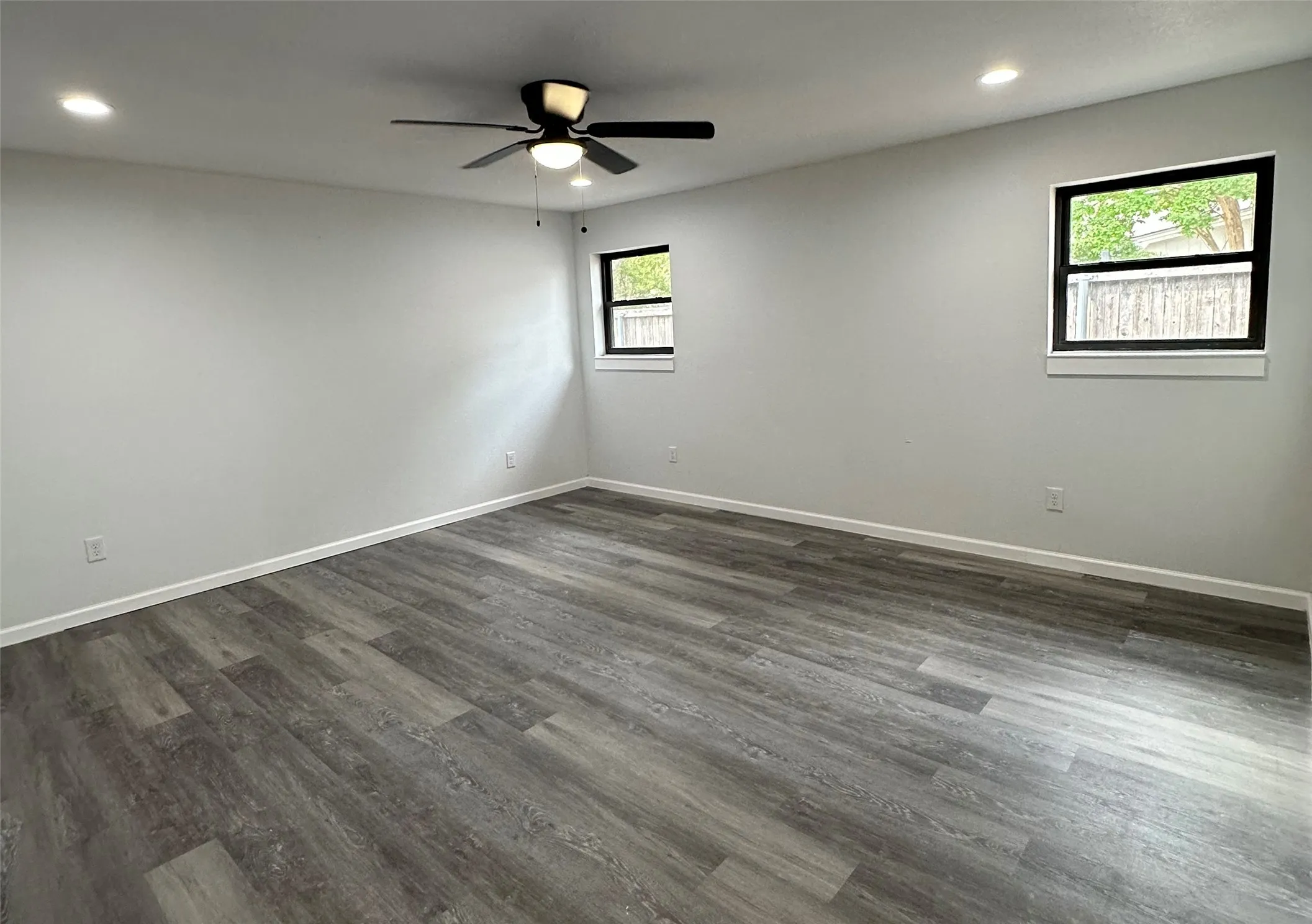 Wood-finish flooring, recessed lighting, ceiling fan with light, and multiple windows with black trim