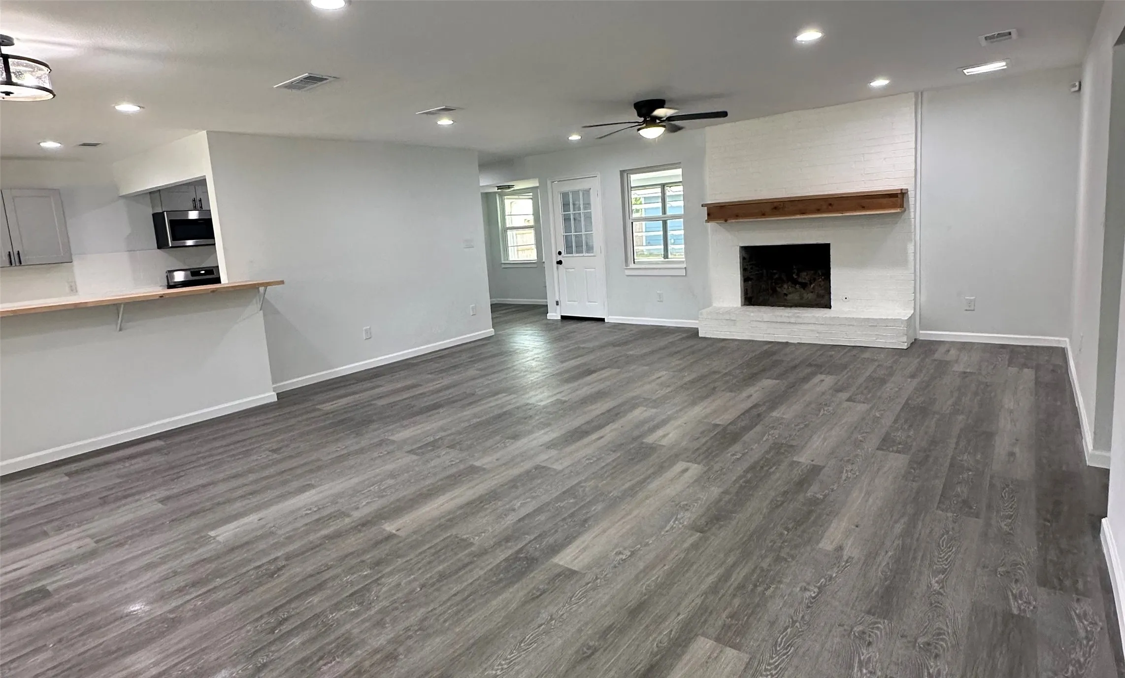 Spacious living area featuring wood-finish flooring, a white brick fireplace with a wood mantle, a ceiling fan, and recessed lighting