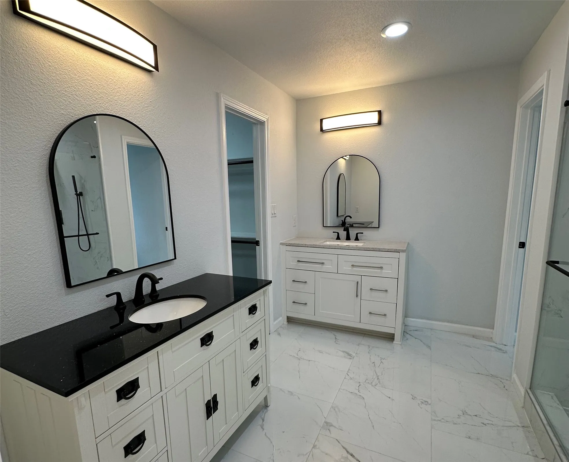 Dual vanity with dark countertops, white cabinetry, and arched mirrors
