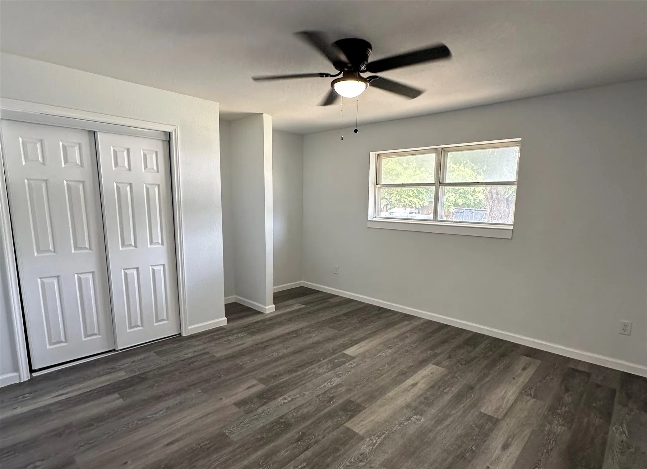 Wood-finish flooring, white walls, double-pane window, ceiling fan with integrated lighting, and bi-fold closet doors