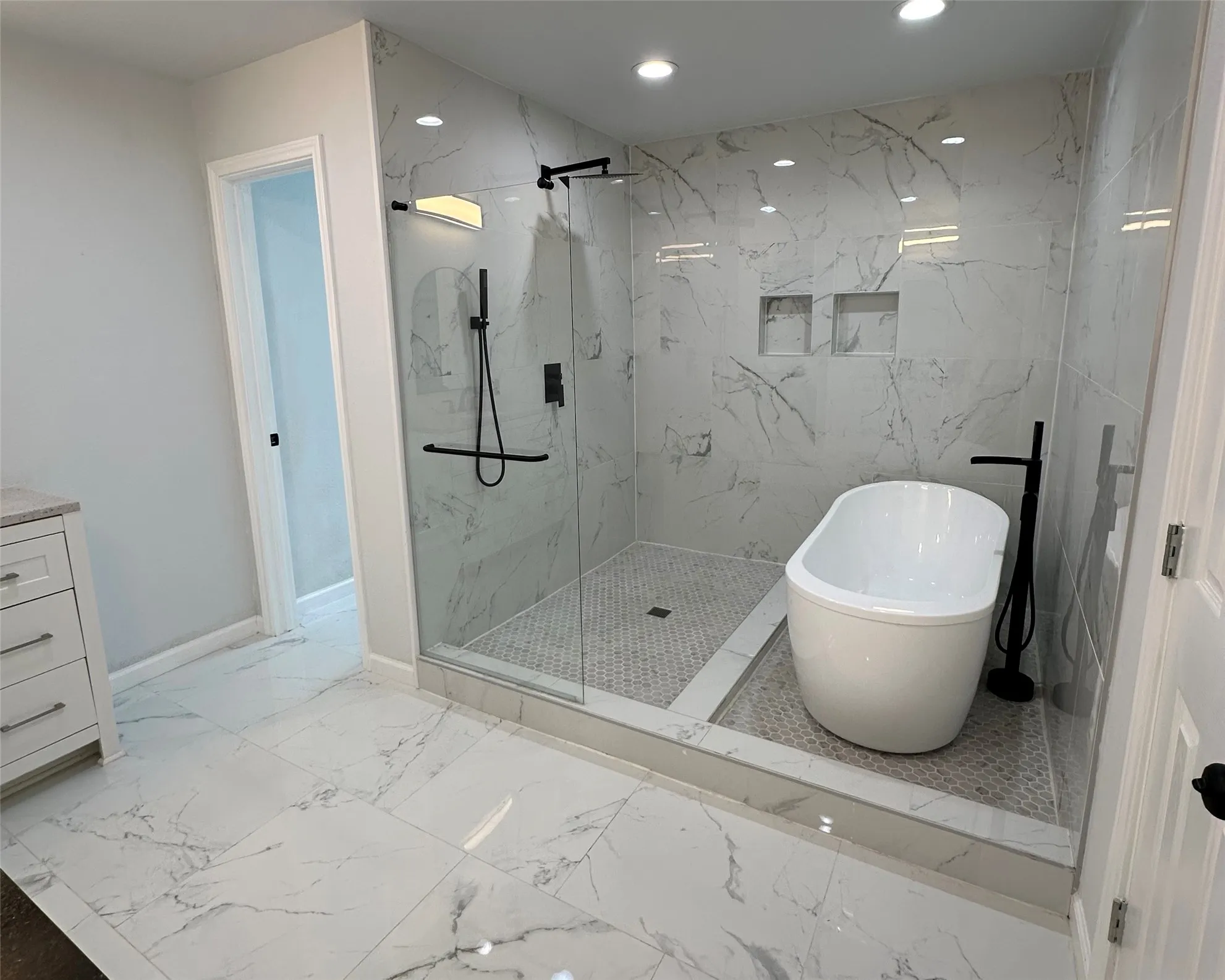 Walk-in shower featuring a freestanding tub, matte black fixtures, and built-in wall niches