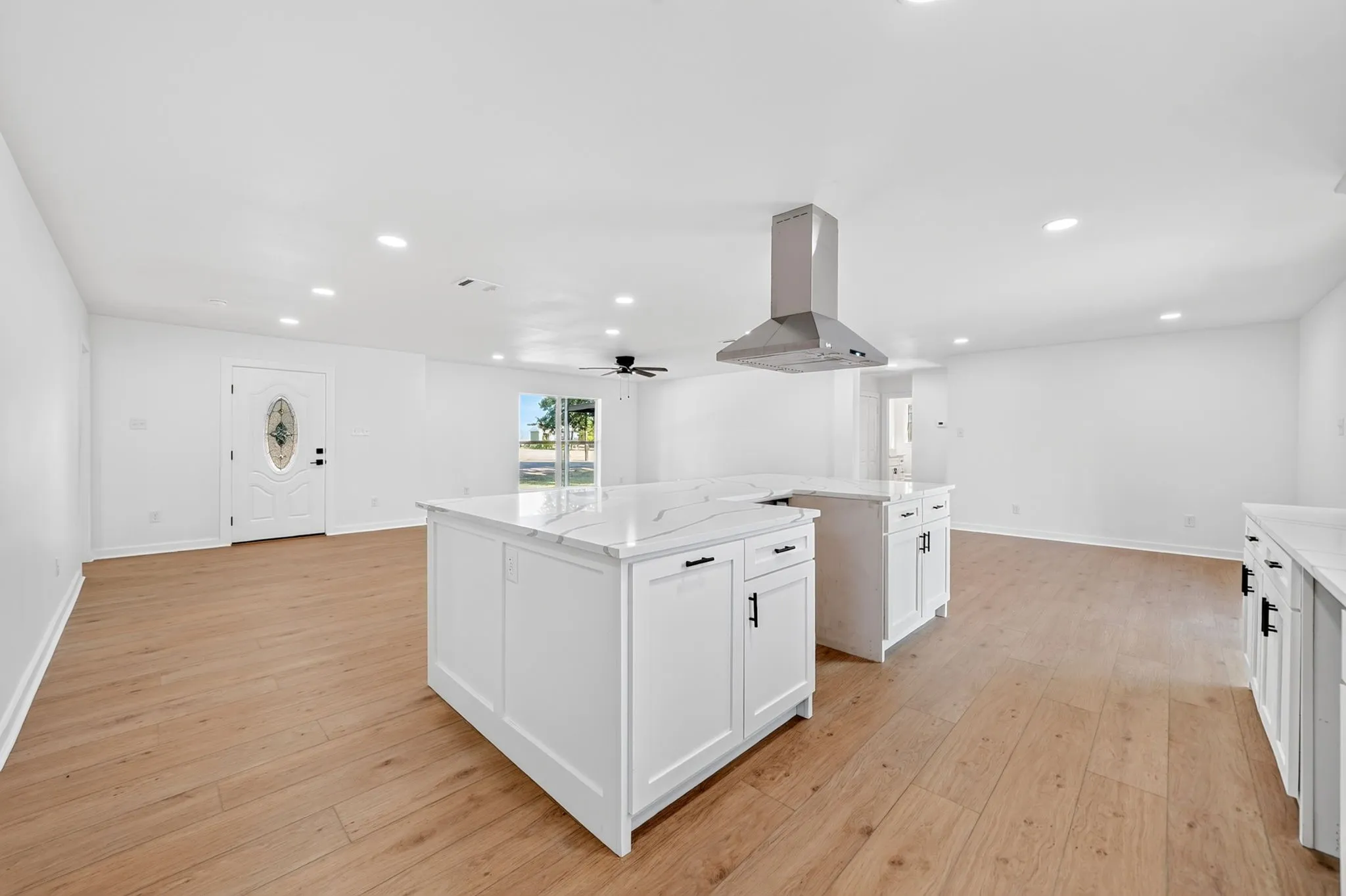 Open-concept living area with wood-finish flooring, recessed lighting, and a decorative front door