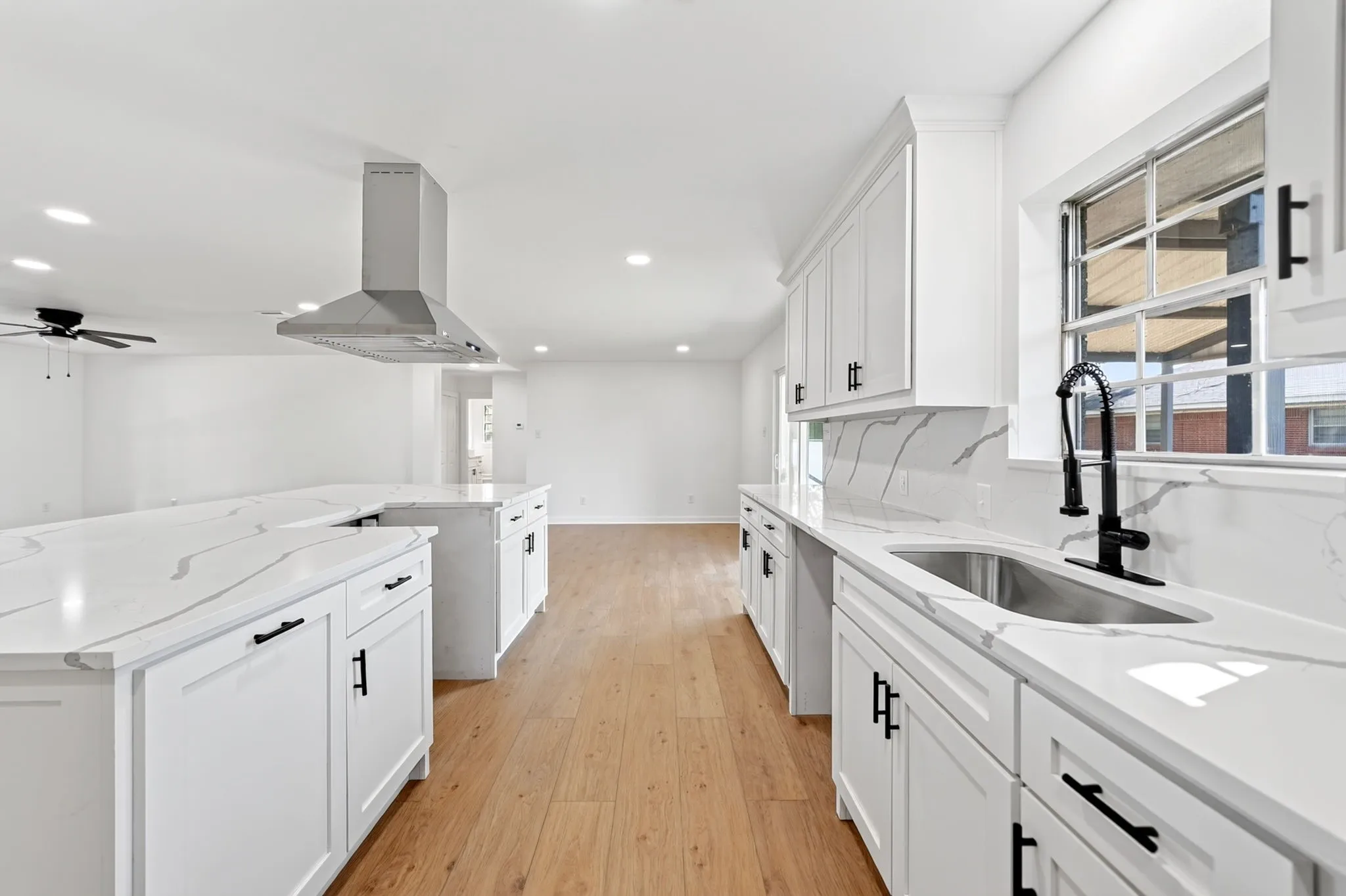 Kitchen featuring white cabinetry, light-toned wood-finish flooring, white countertops with integrated backsplash, a stainless steel sink with a black faucet, and a stainless steel range hood