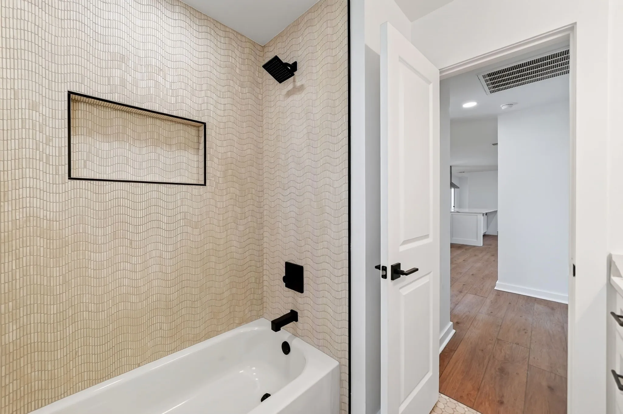 Bathtub with wave-patterned tile surround, matte black fixtures, and built-in shower niche