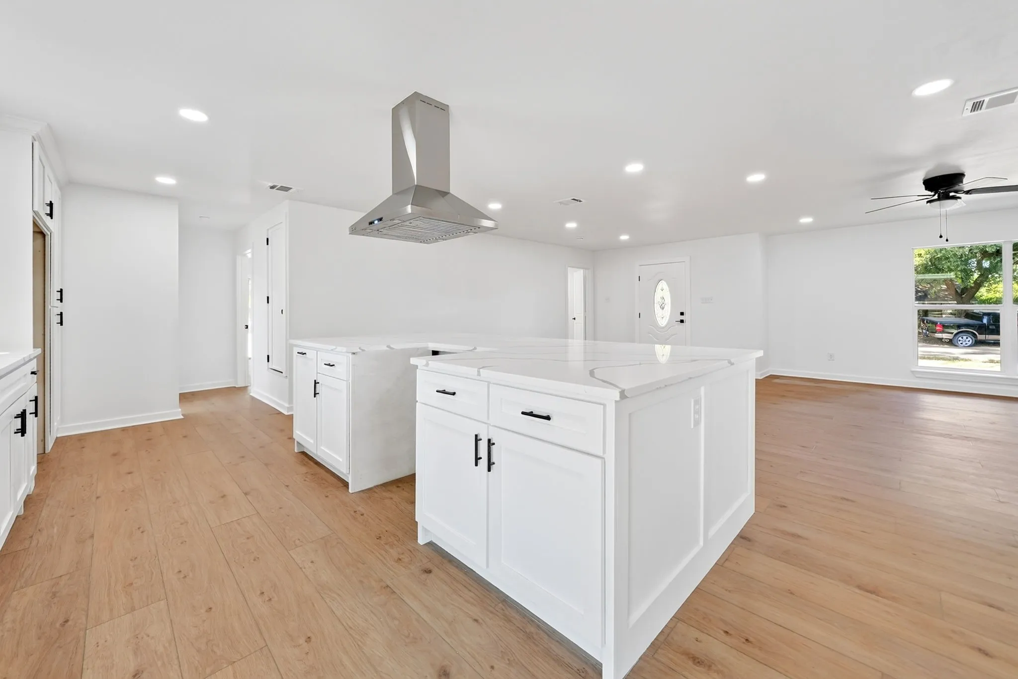 Open-concept living area featuring wood-finish flooring, white cabinetry, a stainless steel range hood, recessed lighting, and a ceiling fan
