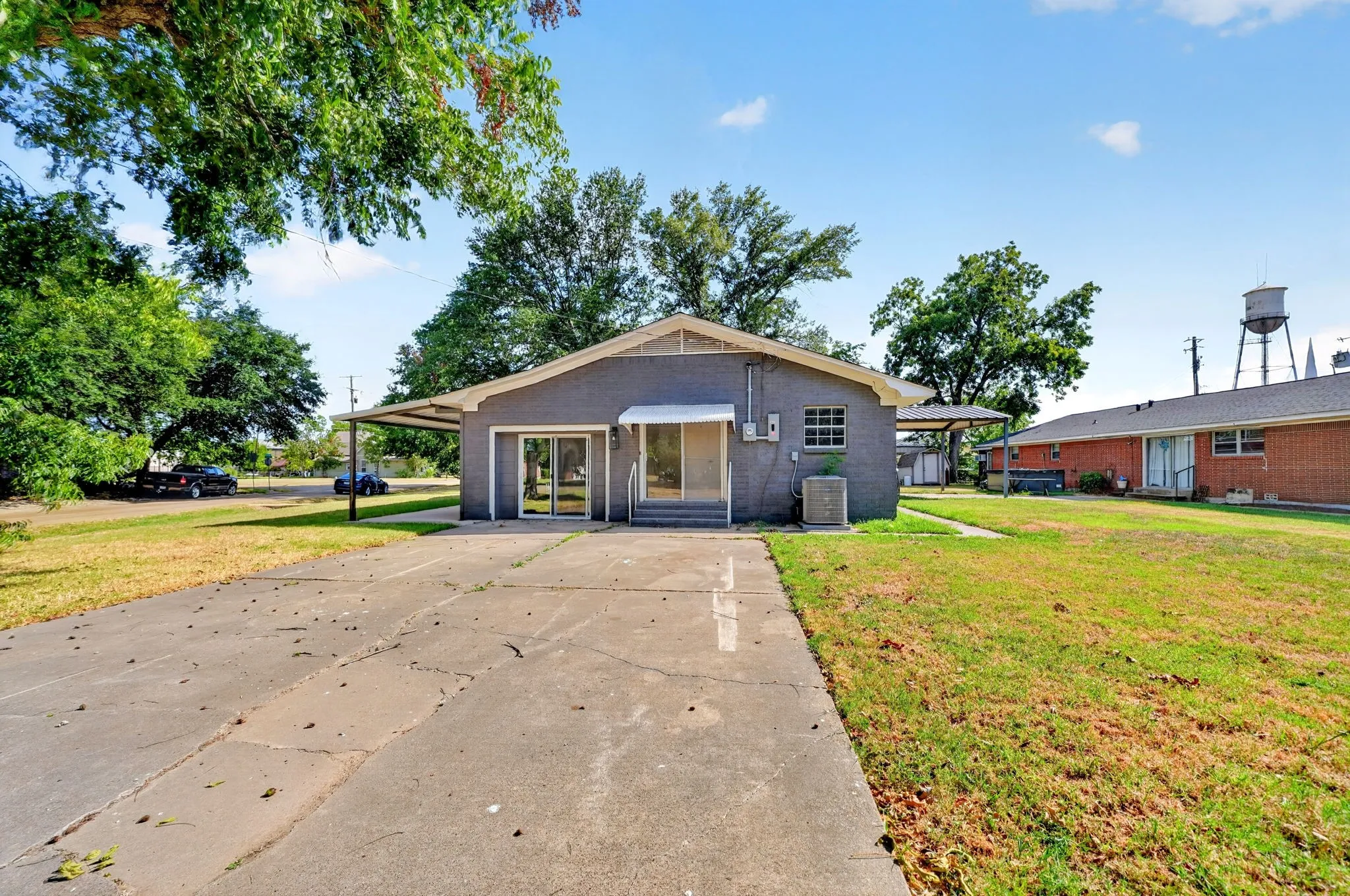Exterior featuring a gray stucco finish, two carport structures, a concrete driveway, and a partially covered entry