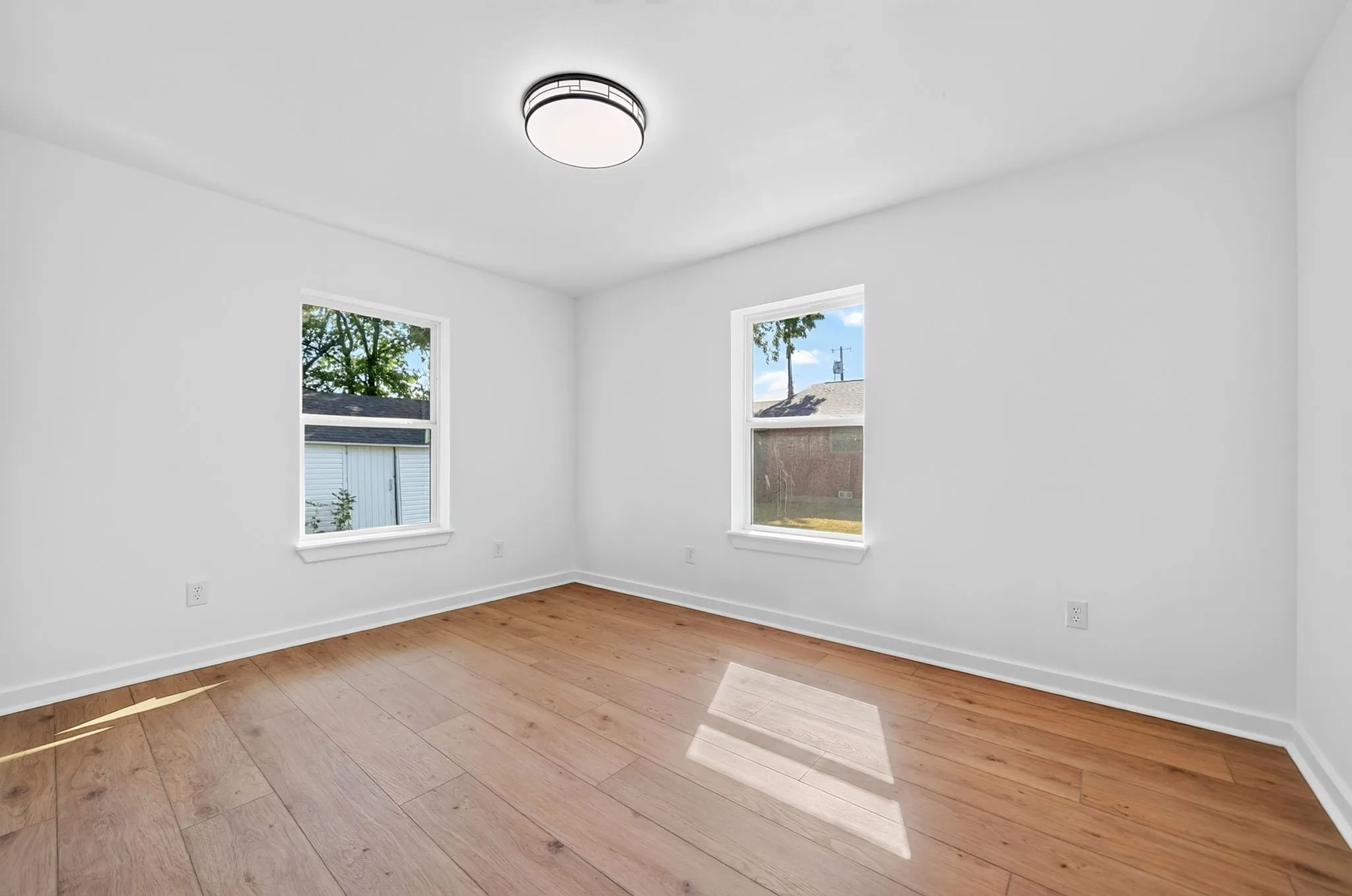 Wood-finish flooring, white walls, two windows, and a flush-mount ceiling light