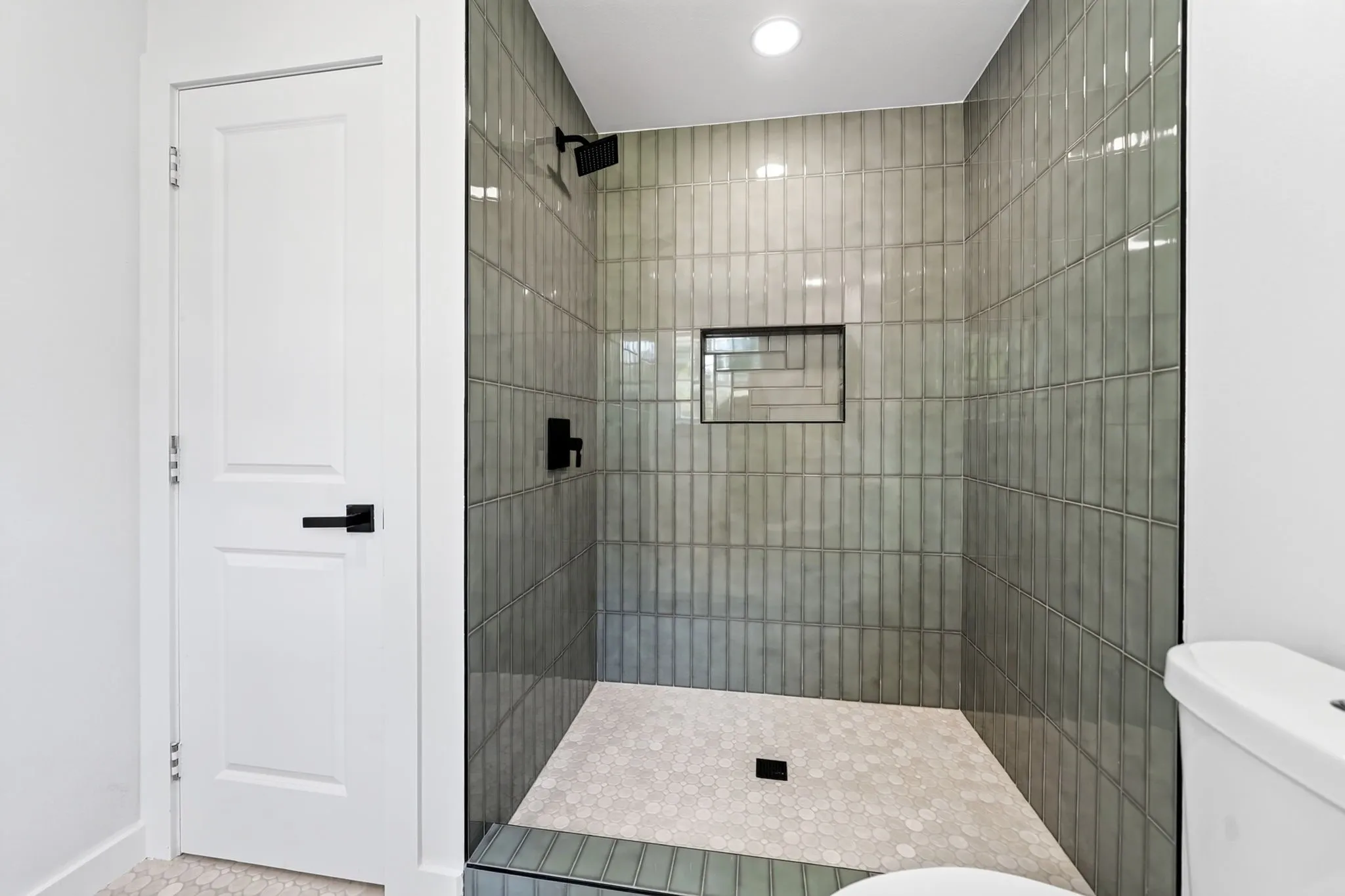 Walk-in shower with vertical subway tile, glass enclosure, recessed niche, and matte black fixtures