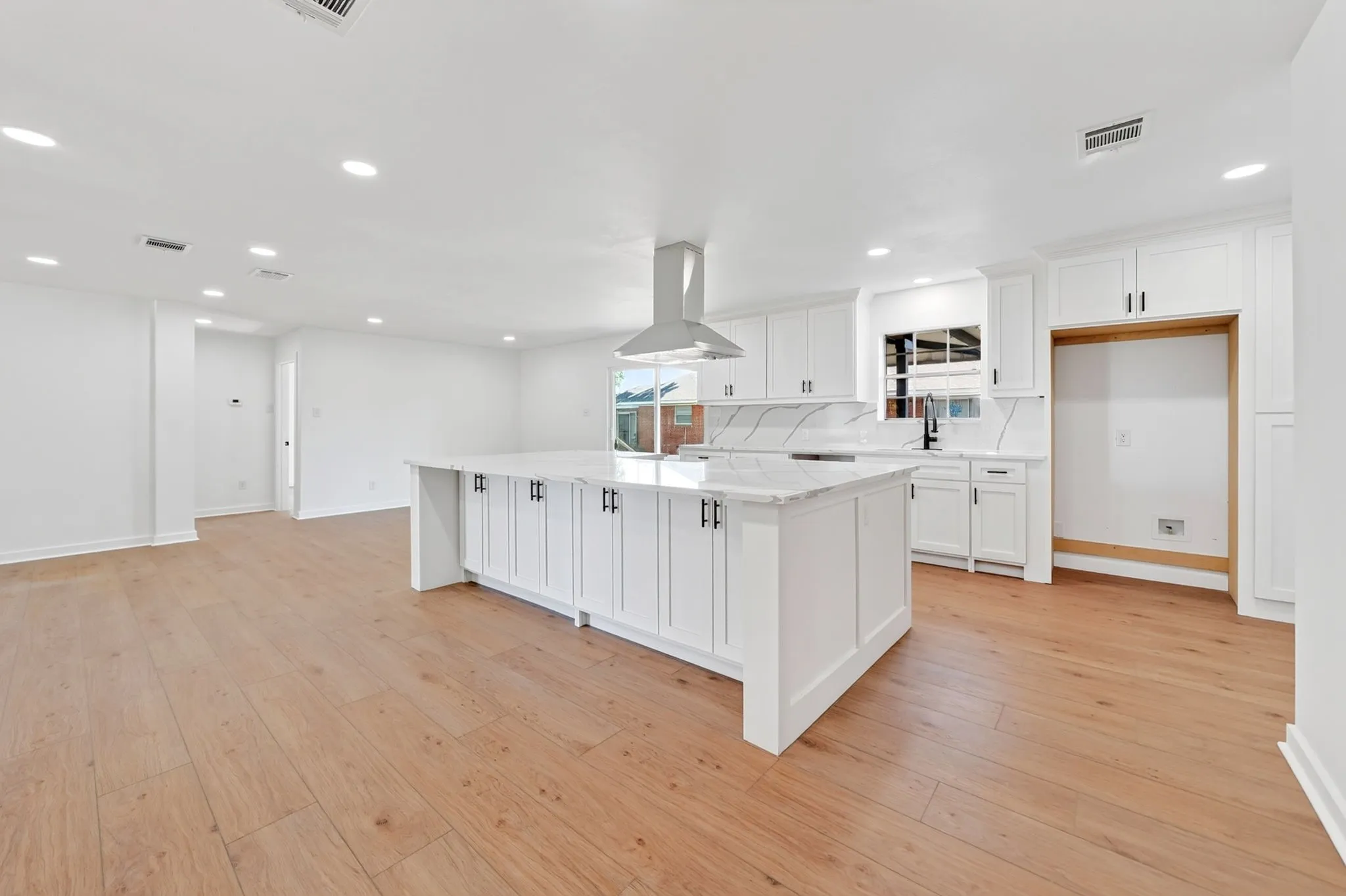 Kitchen featuring white cabinetry, a central island with a light-colored countertop, recessed lighting, wood-finish flooring, and a stainless steel range hood