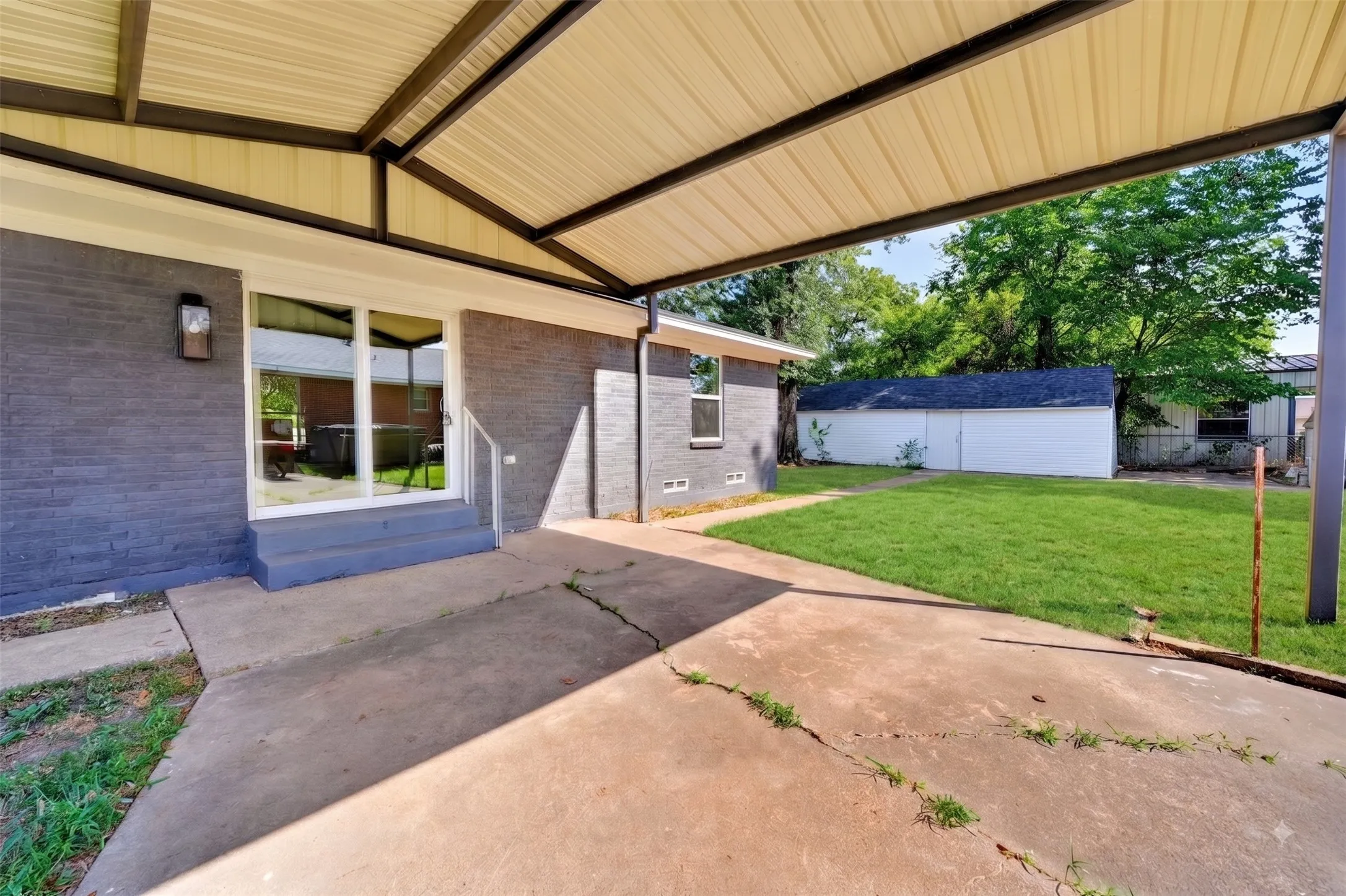 Covered patio with modern metal beam framework overlooking a spacious lawn with mature landscaping