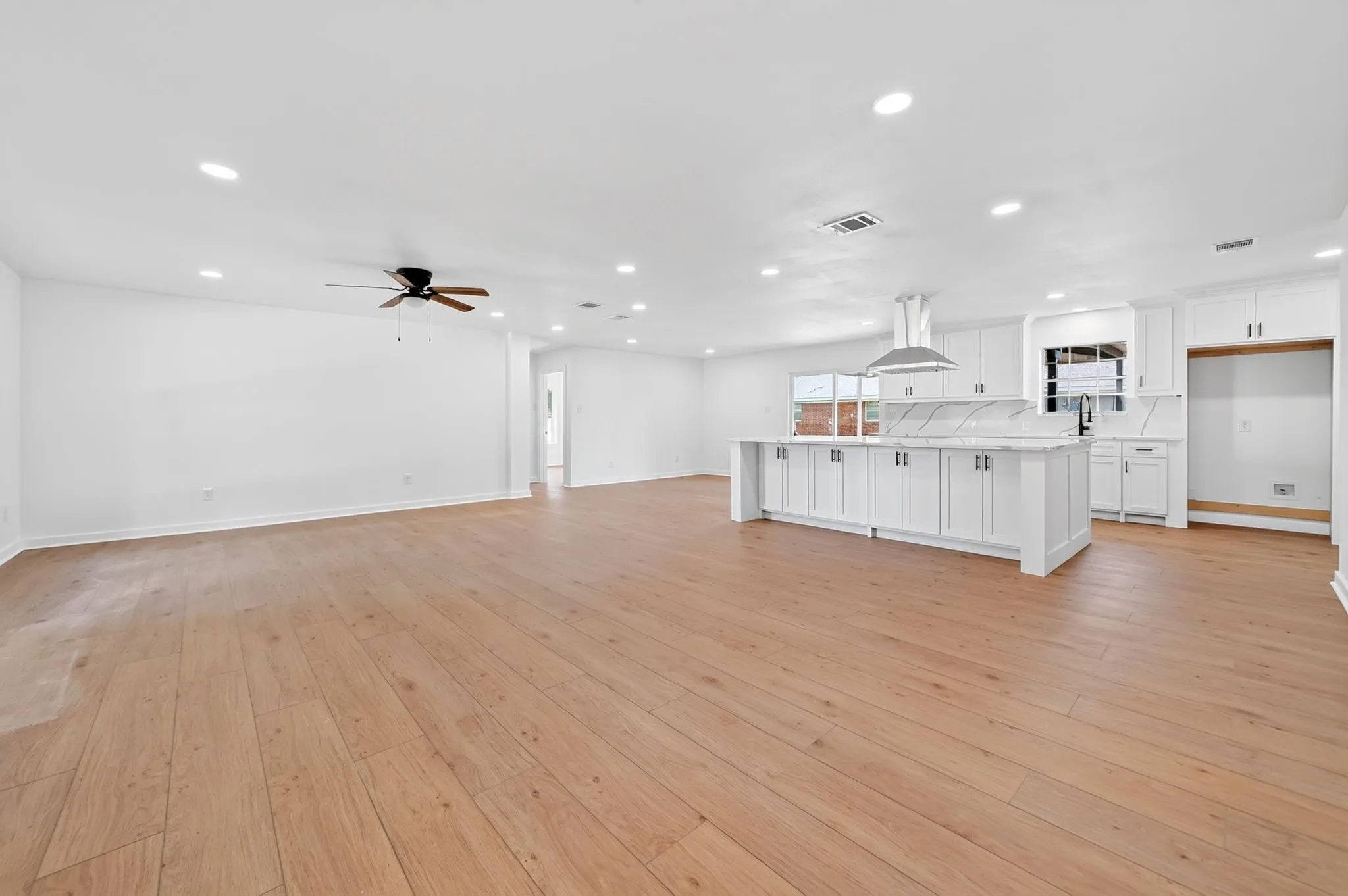 Expansive open-concept living area with wood-finish flooring, recessed lighting, and a ceiling fan
