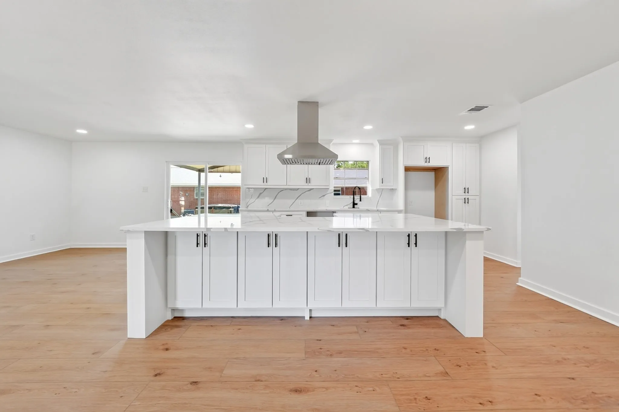 Spacious kitchen featuring an expansive center island, white cabinetry, integrated range hood, and wood-finish flooring