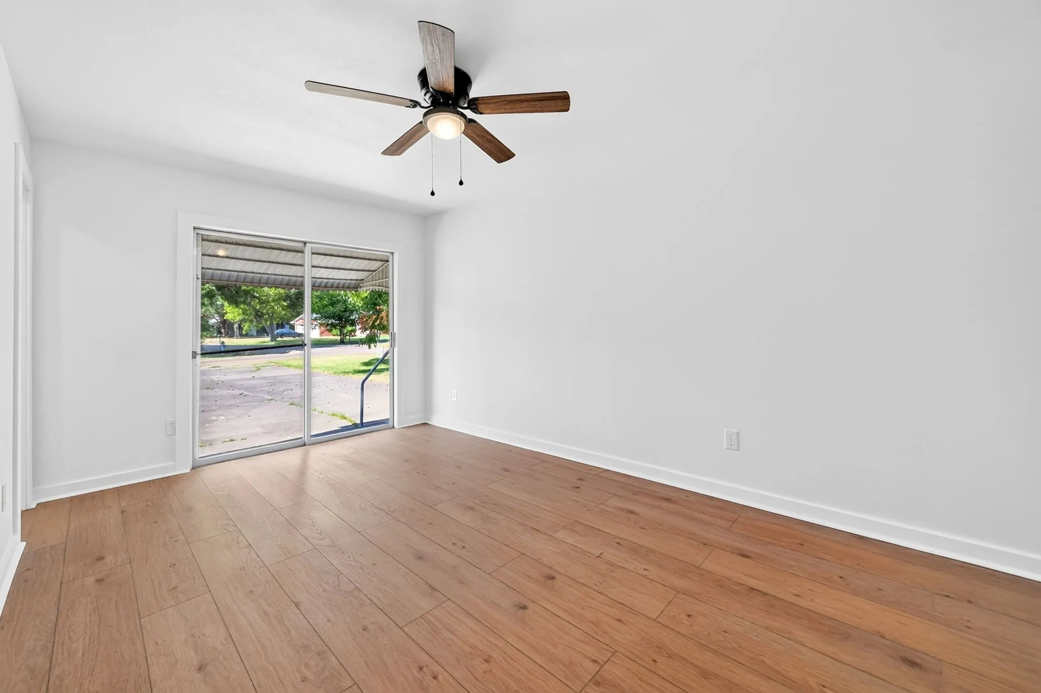 Wood-finish flooring, white walls, ceiling fan with integrated lighting, and sliding glass door