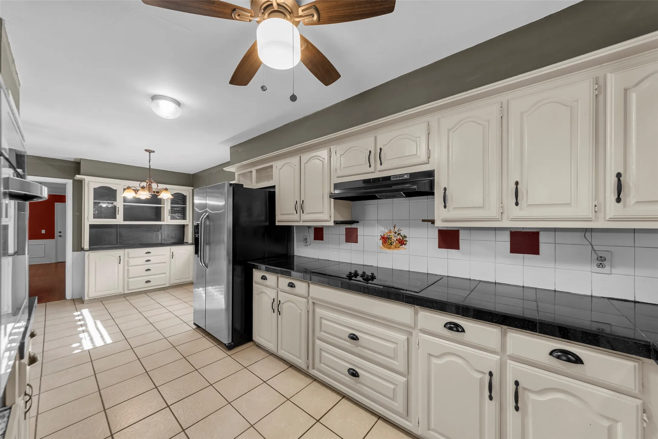 Kitchen with white cabinetry, black countertops, tile flooring, and a stainless steel refrigerator