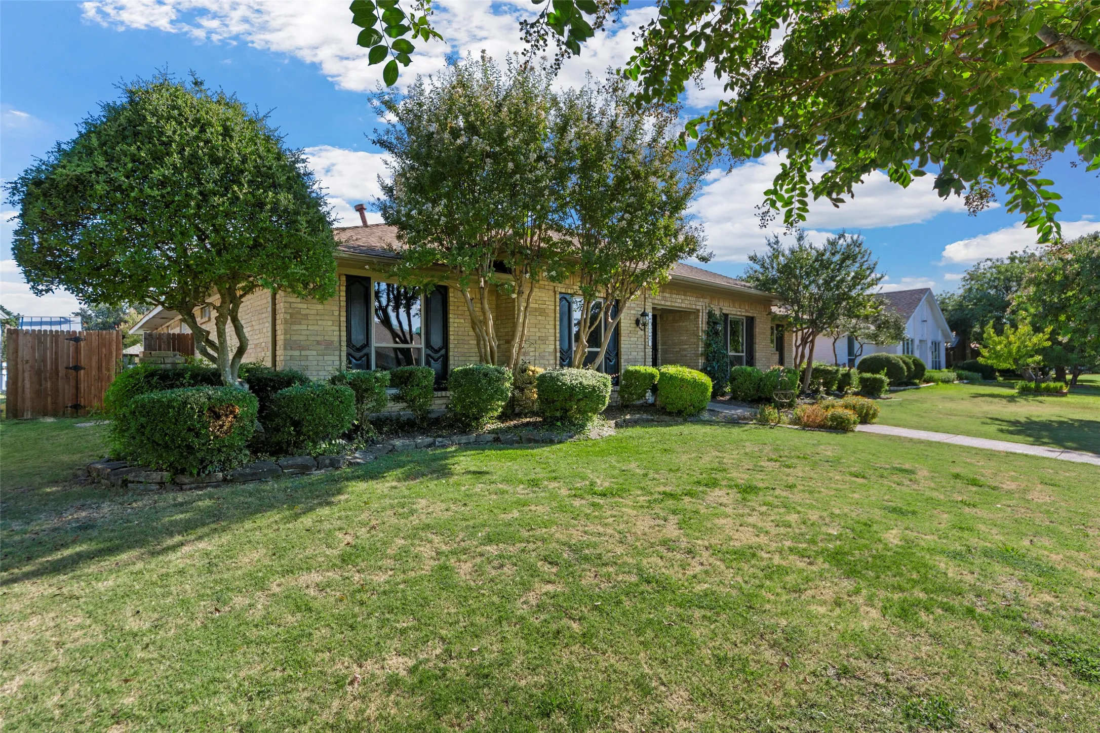 Brick exterior with dark shutters, established landscaping, and a fenced side yard