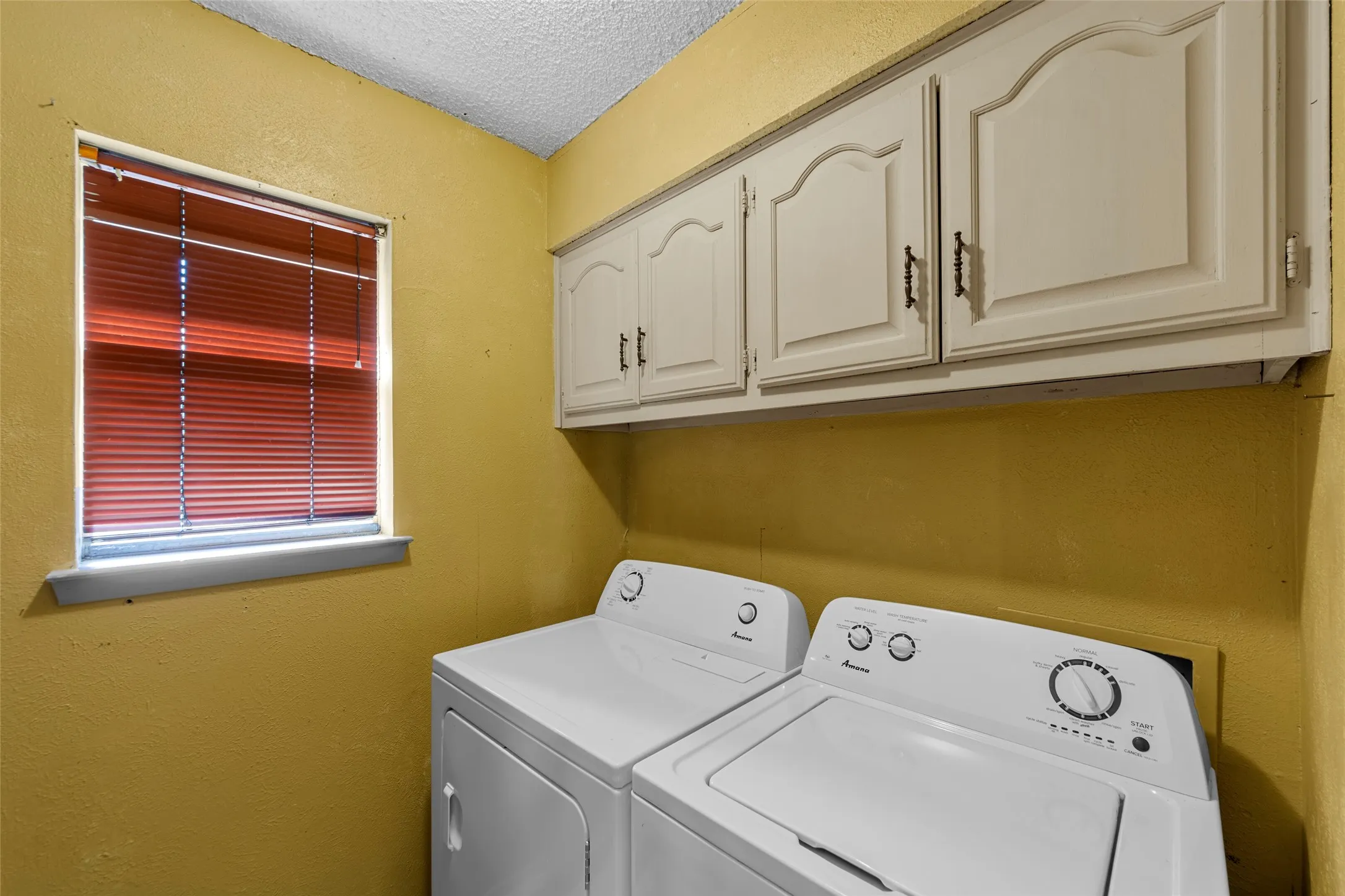 Dedicated laundry area with upper cabinetry and a window