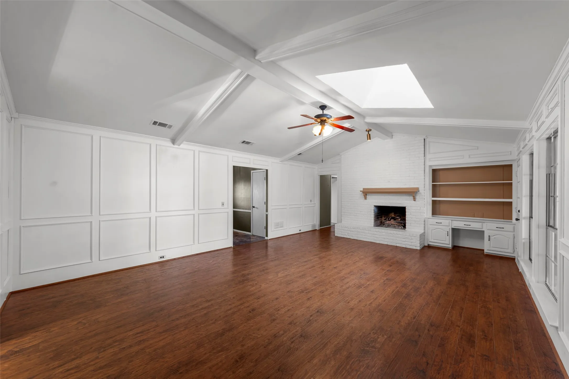 Spacious living area featuring wood-finish flooring, a vaulted ceiling with exposed beams, and a skylight