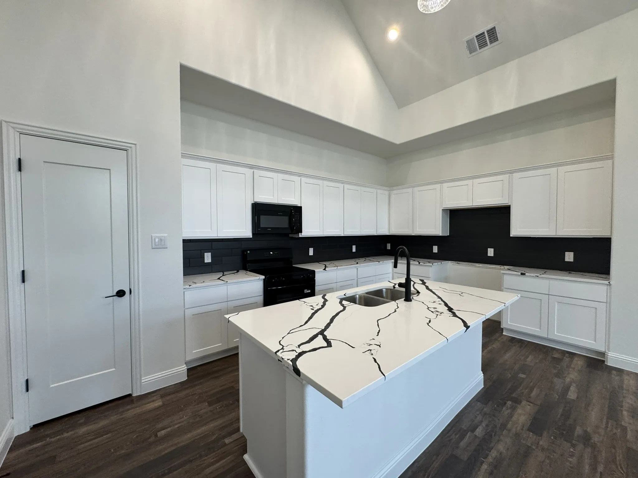 Kitchen featuring vaulted ceilings, wood-finish flooring, white cabinetry, a dark subway tile backsplash, and an island with an undermount double sink