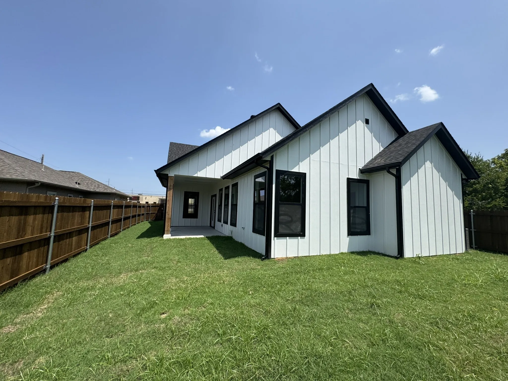 Board and batten exterior with black trim windows, black gutters, and a covered back patio with wood-wrapped columns