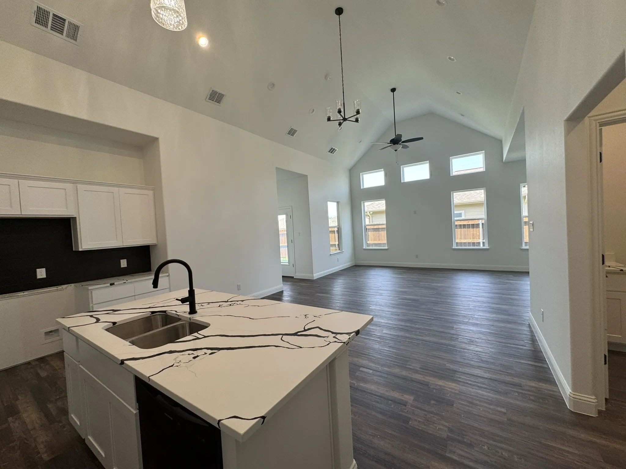 Open-concept living space featuring a vaulted ceiling with exposed beams, wood-finish flooring, a kitchen island with an undermount sink, and recessed lighting