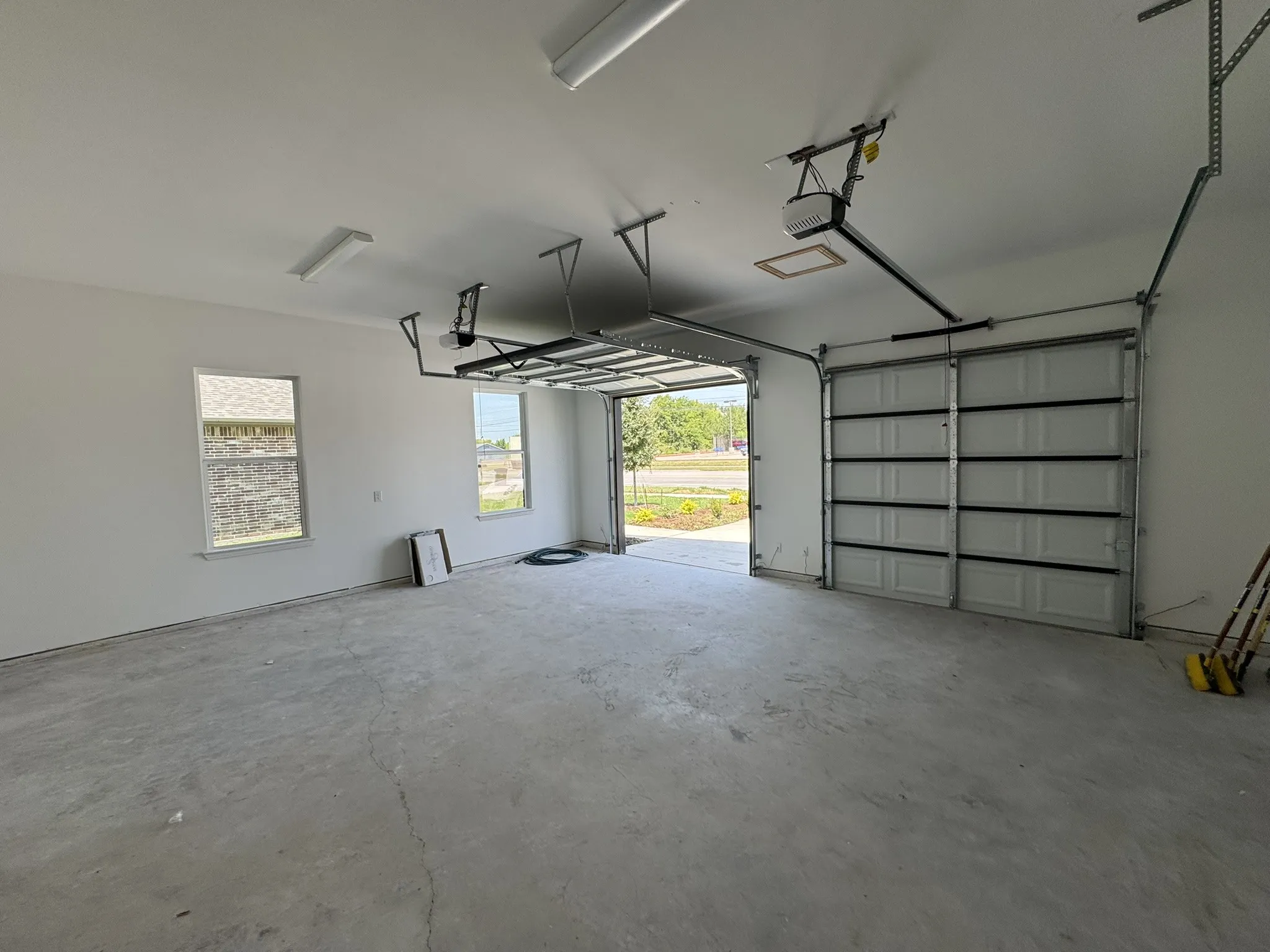 Spacious garage with two automatic overhead doors, concrete flooring, dual window openings, and fluorescent ceiling lighting