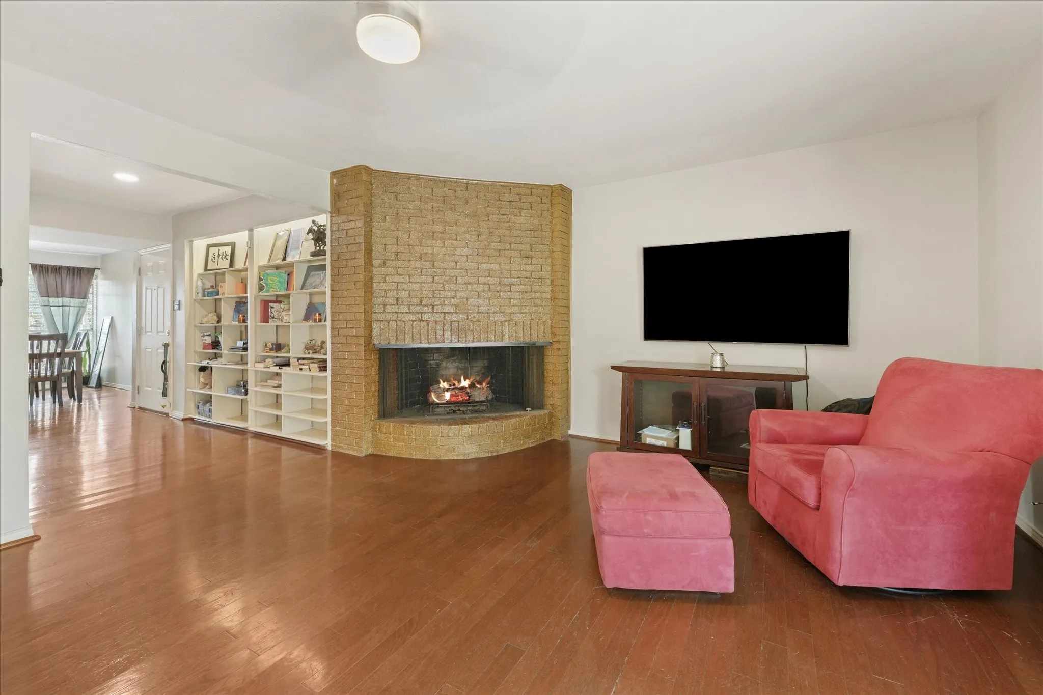 Wood-finish flooring throughout, brick-clad fireplace, and built-in shelving