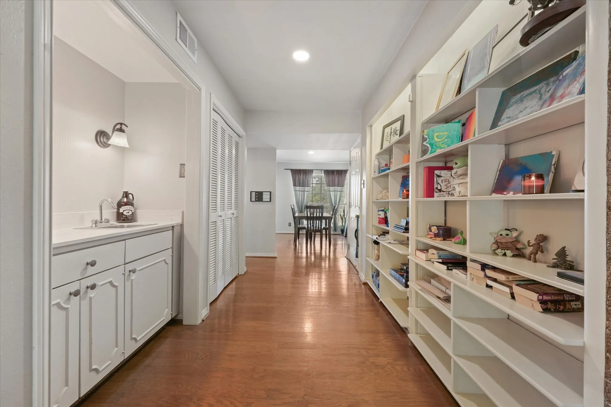 Wood-finish flooring throughout, featuring a built-in wet bar with white cabinetry and countertop, and extensive built-in shelving