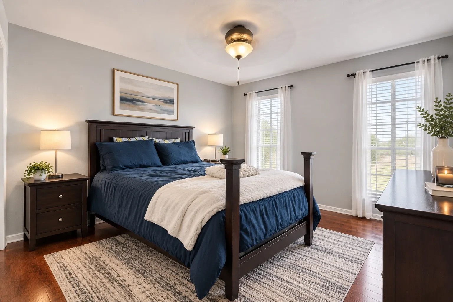 Virtually staged Hardwood flooring, light gray wall color, two windows with blinds, and an overhead light fixture