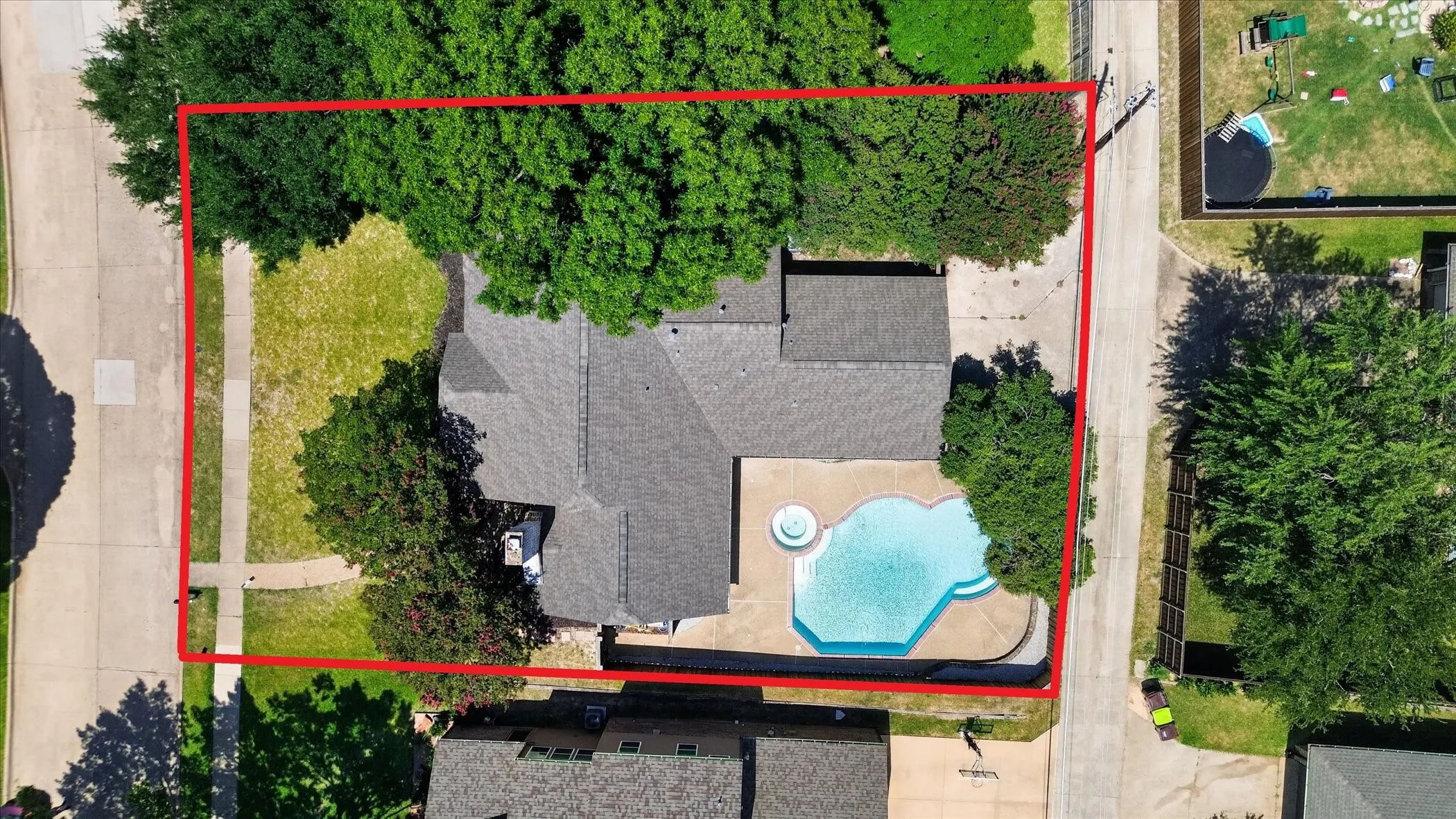Property features a swimming pool with an attached spa, a concrete pool deck, a shingled roof, a paved driveway, and mature landscaping