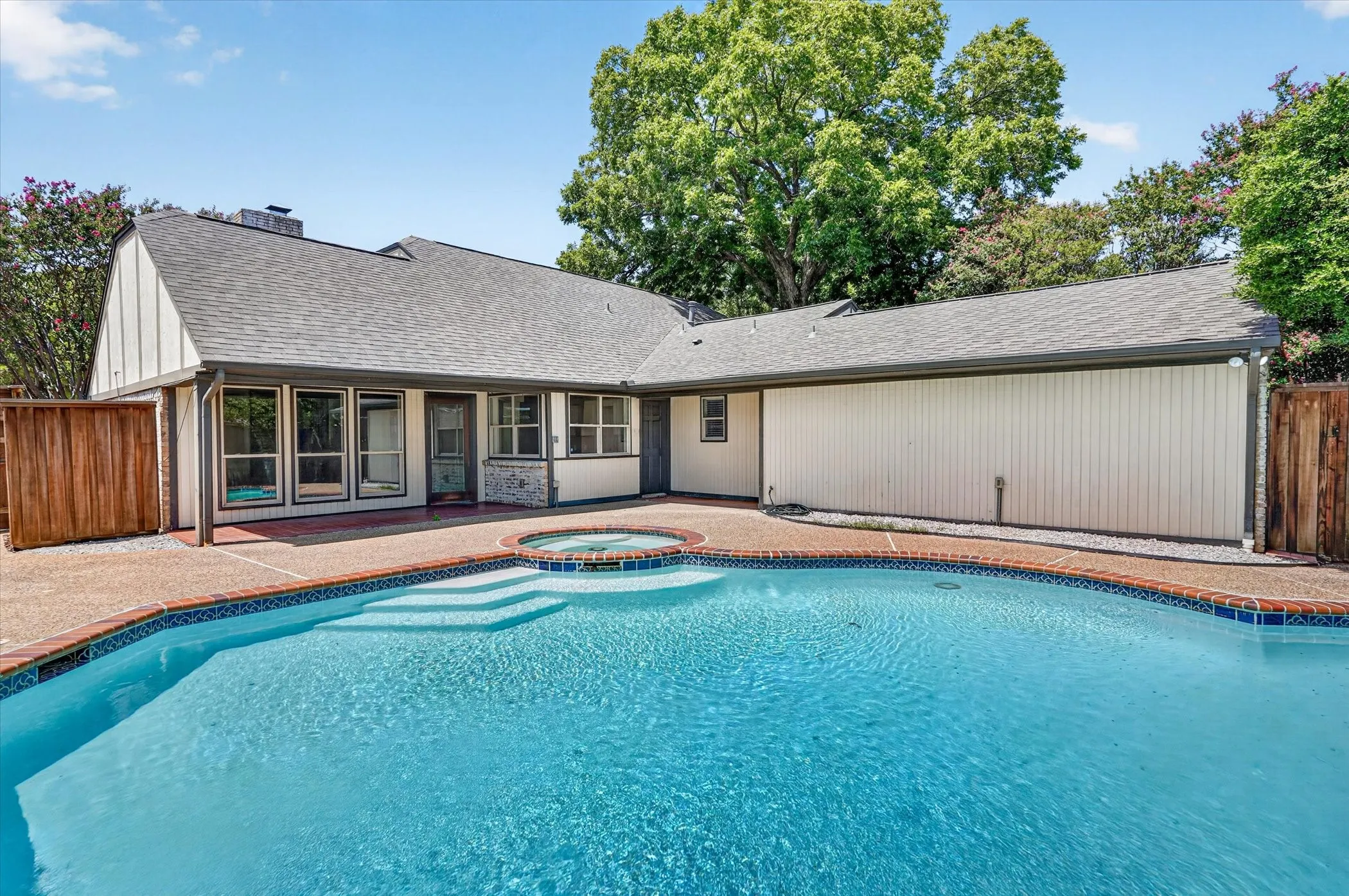 Exterior featuring a blue-tiled swimming pool with integrated steps, a circular spa, and a textured concrete pool deck