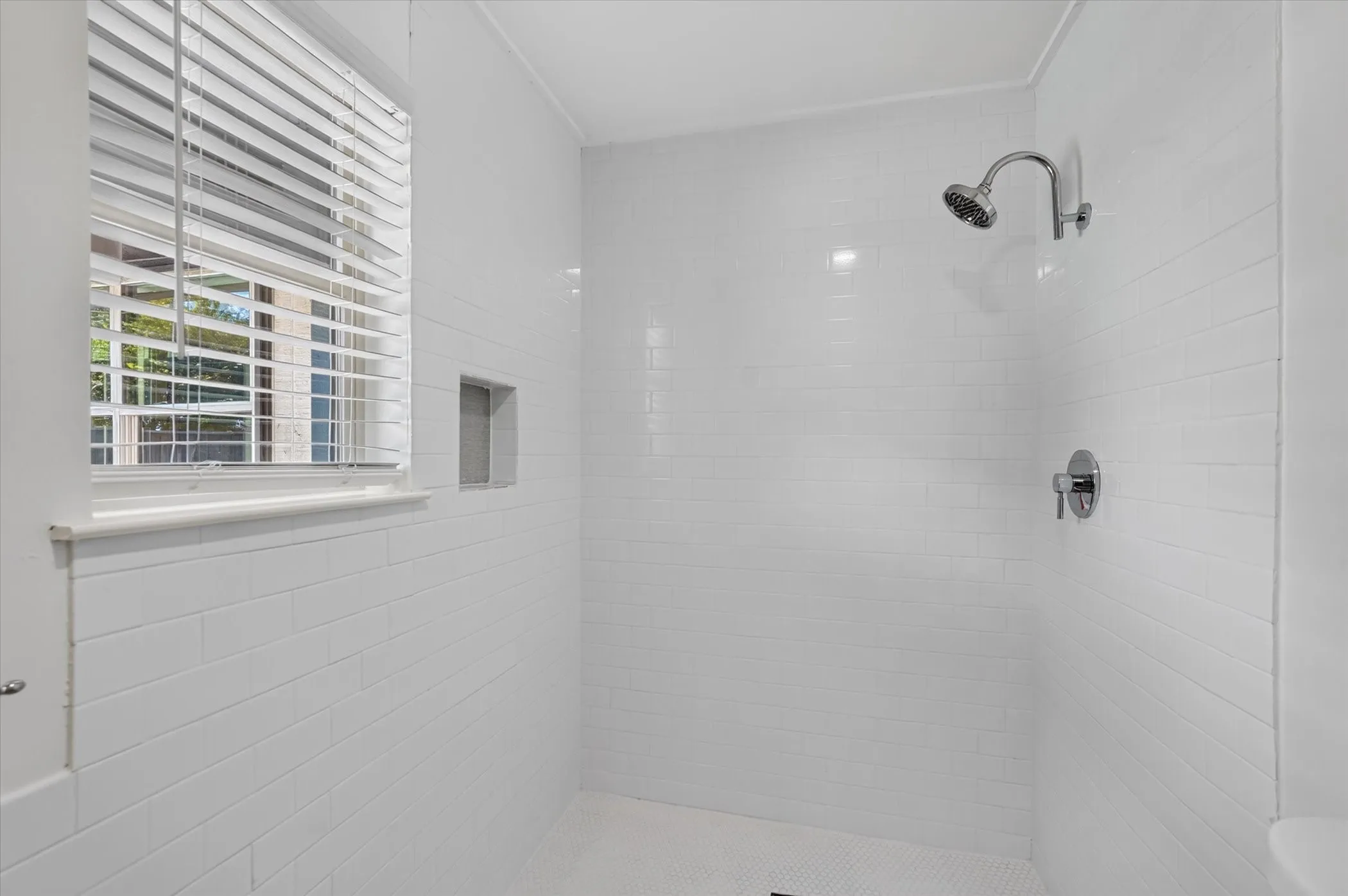 Walk-in shower with white subway tile, a built-in niche, and a window with blinds