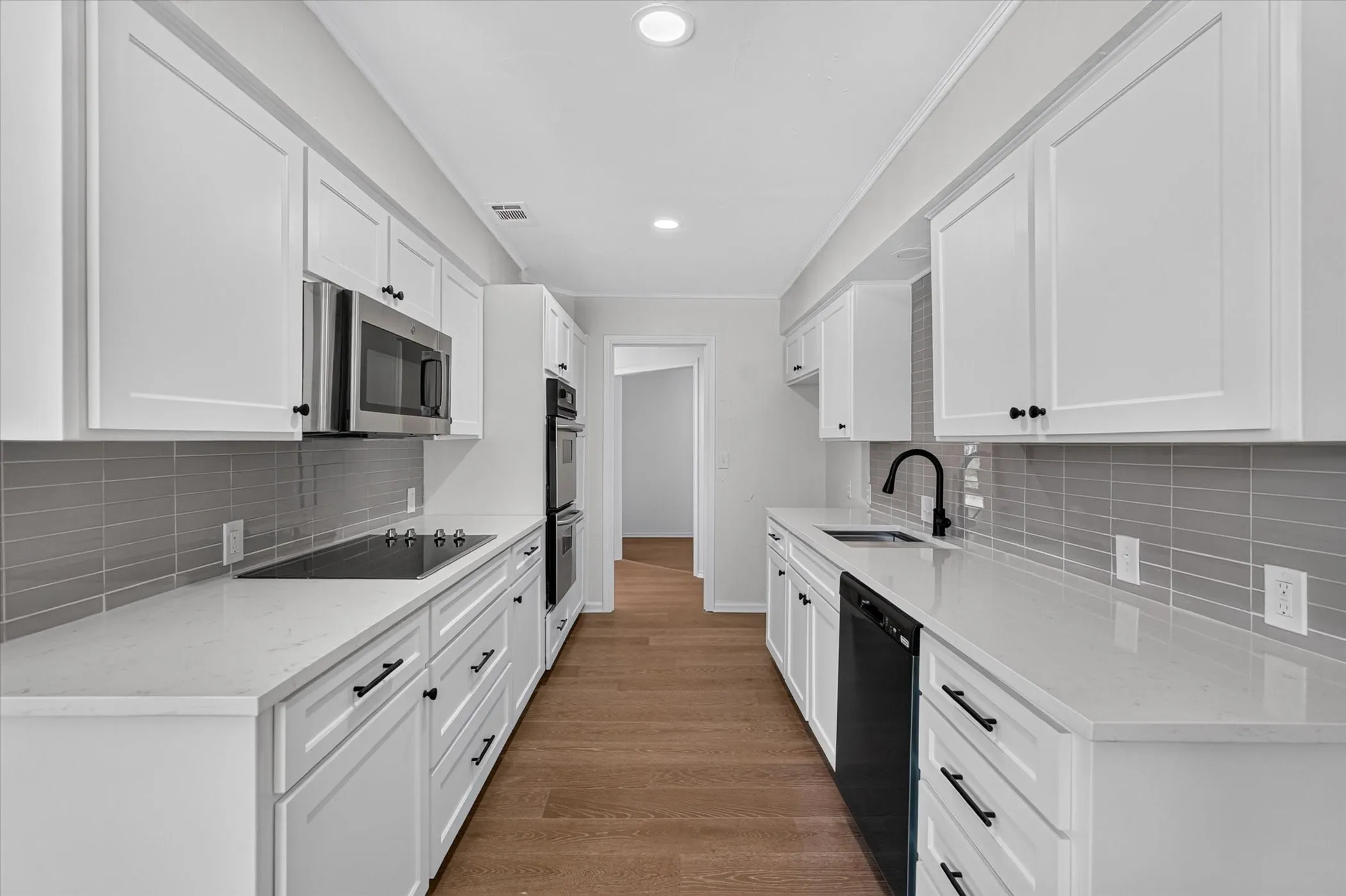 White cabinetry with dark hardware, stone countertops, a subway tile backsplash, wood-finish flooring, and stainless steel appliances