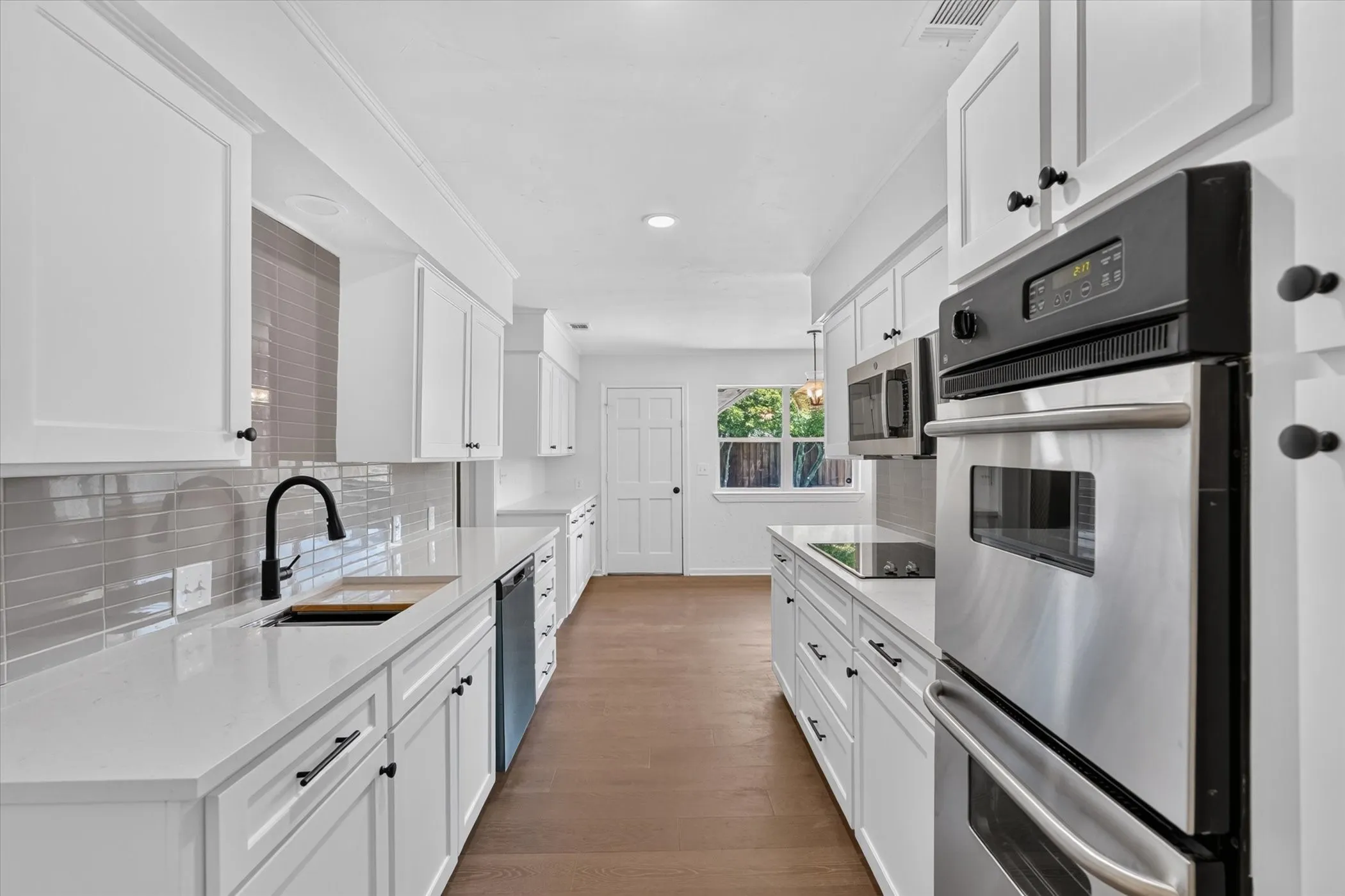 Galley kitchen featuring white cabinetry, light-toned countertops, a stainless steel double oven, and a black faucet