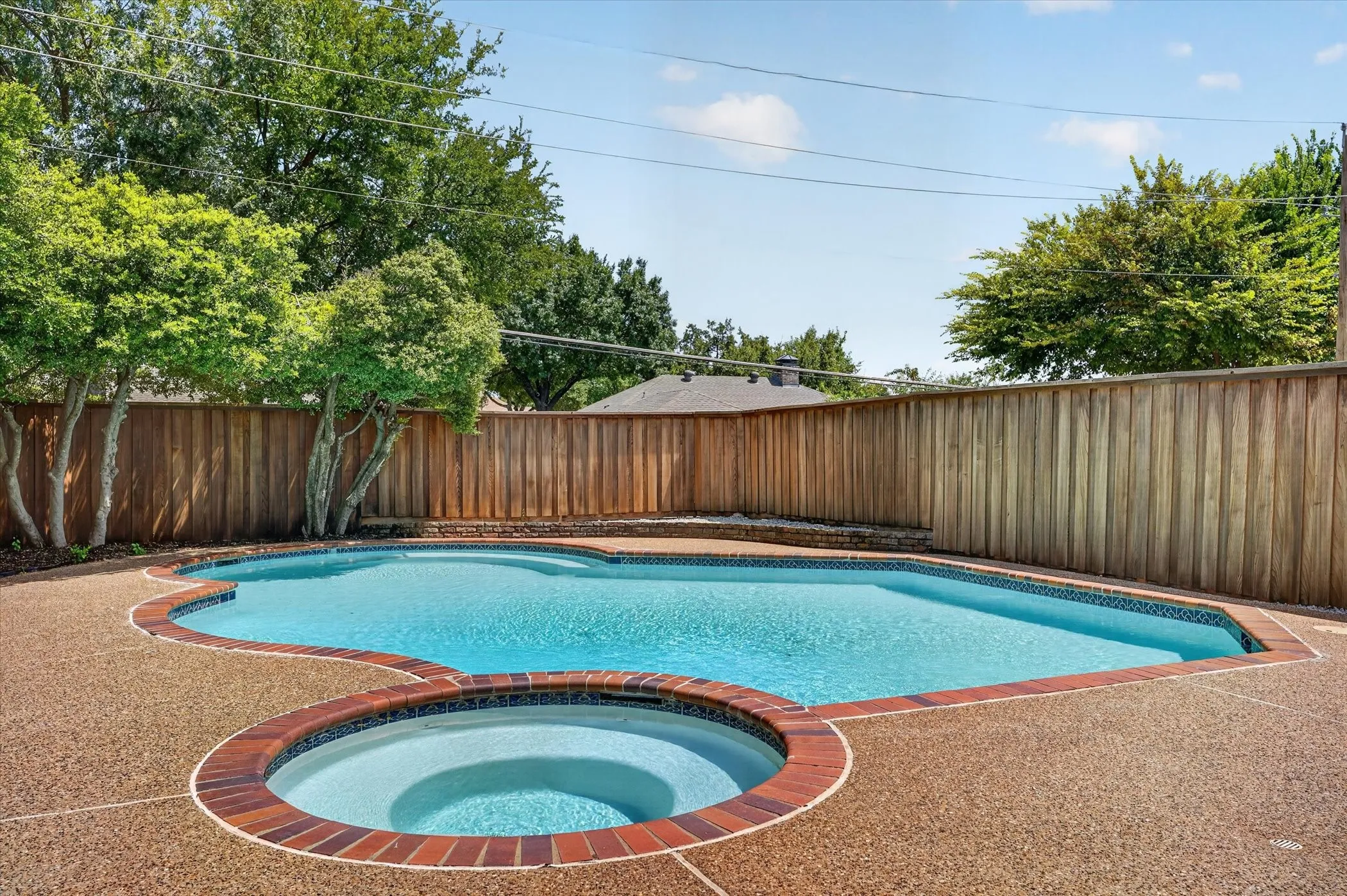 Custom-shaped pool and spa with brick coping and a large aggregate patio