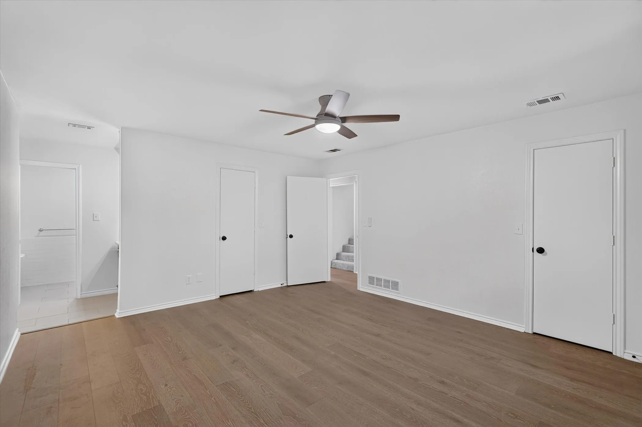 Wood-finish flooring, white painted walls, and a ceiling fan with integrated lighting