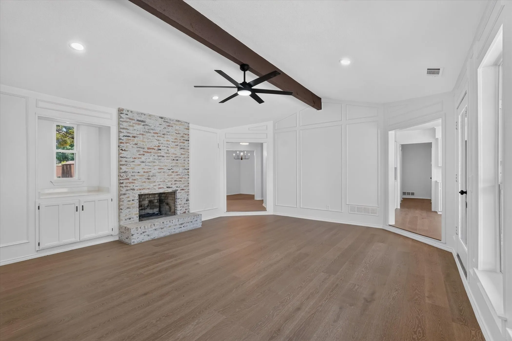 Spacious living area featuring wood-finish flooring, a brick fireplace, built-in cabinetry, decorative wall paneling, and a wood beam ceiling