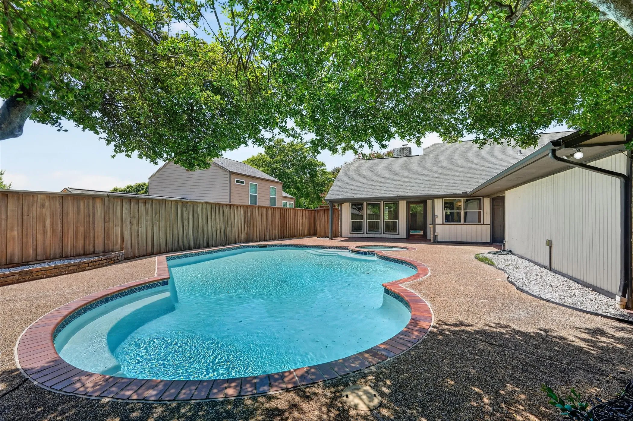 Curved swimming pool with integrated spa and dark brick coping